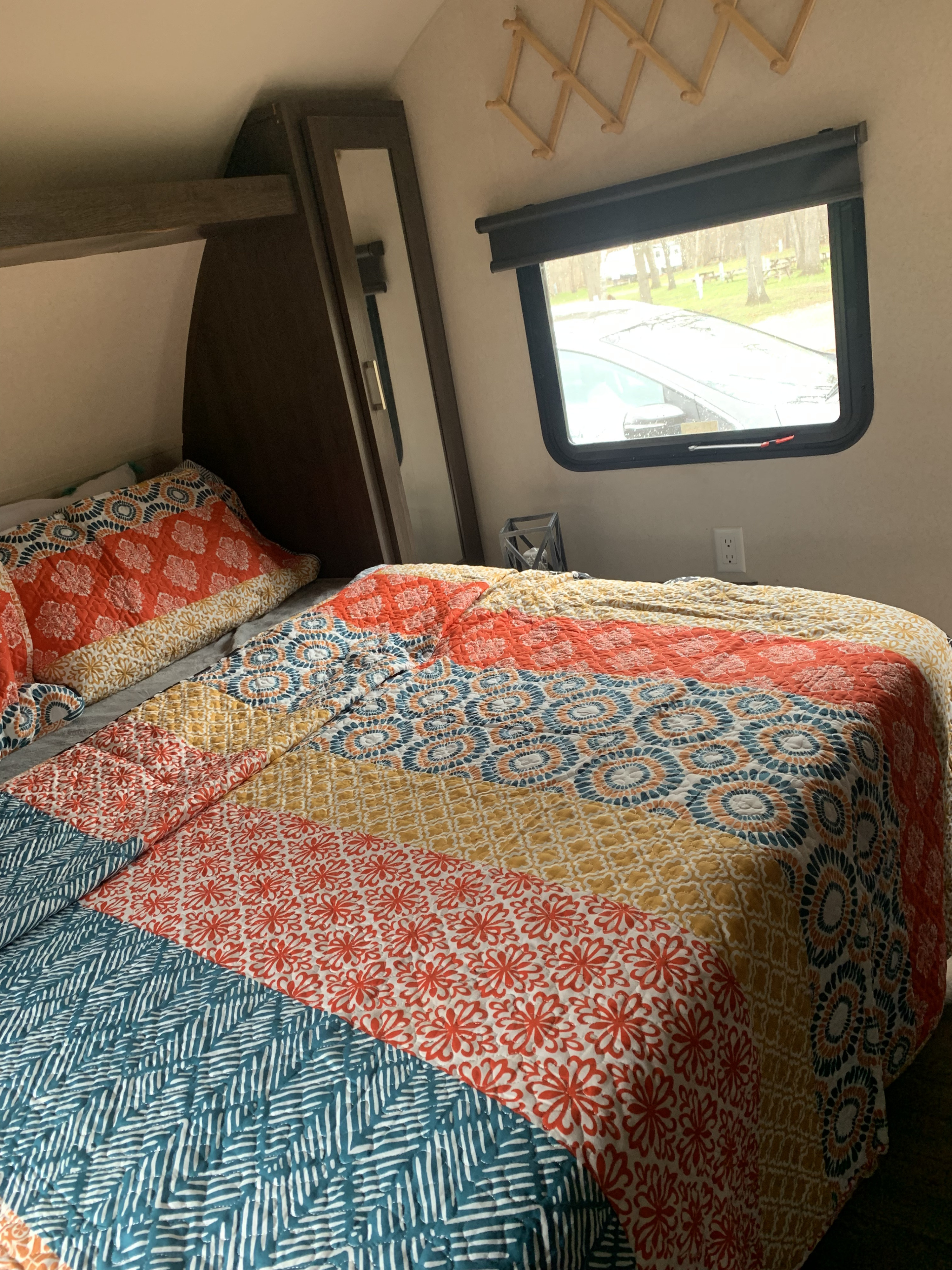 Cozy RV rental bedroom with a colorful quilt, mirror, and window overlooking a tree-lined area.. Forest River Salem Cruise Lite 2018
