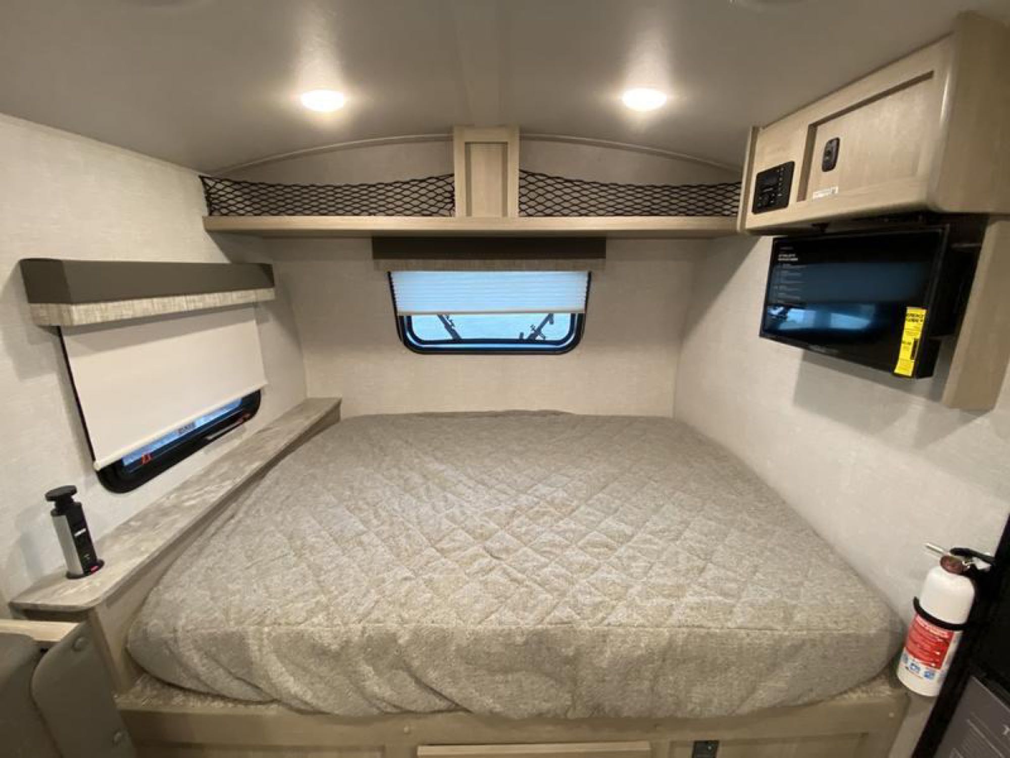 RV rental bedroom featuring a large bed, overhead storage, TV, and window, designed for compact comfort.. Forest River Flagstaff E-Pro 2022