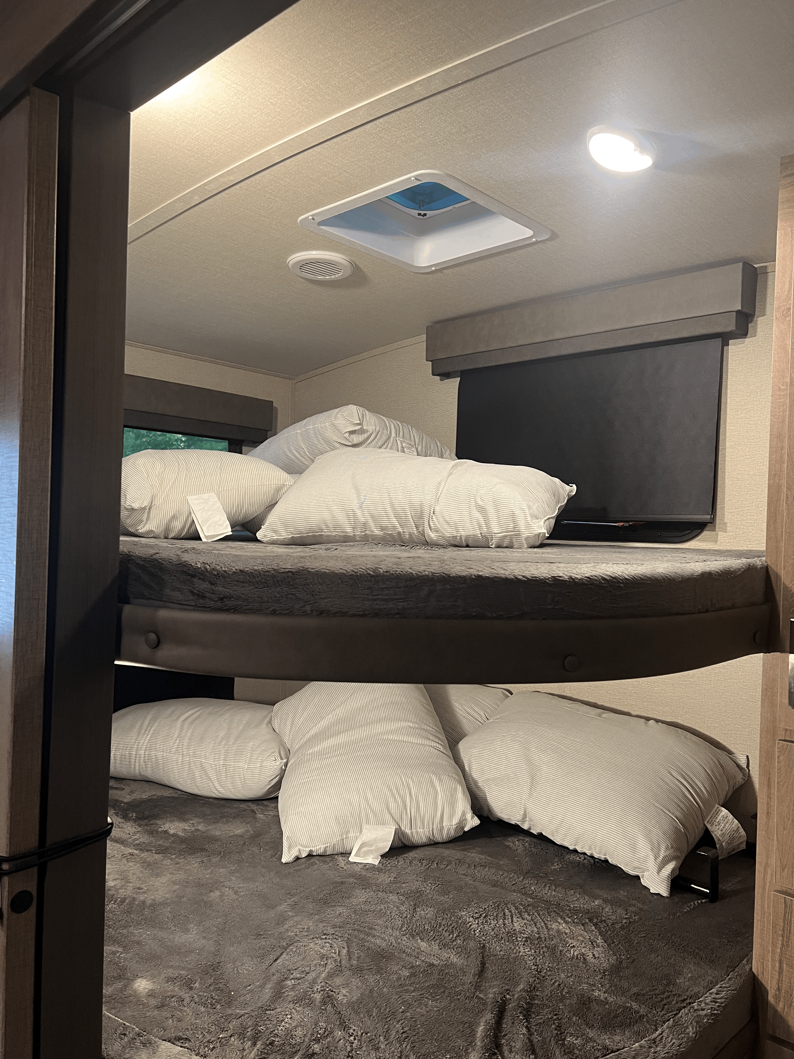 Cozy RV rental bunk beds with striped pillows, dark blankets, & a window for comfortable sleep.. Grand Design Imagine 2022