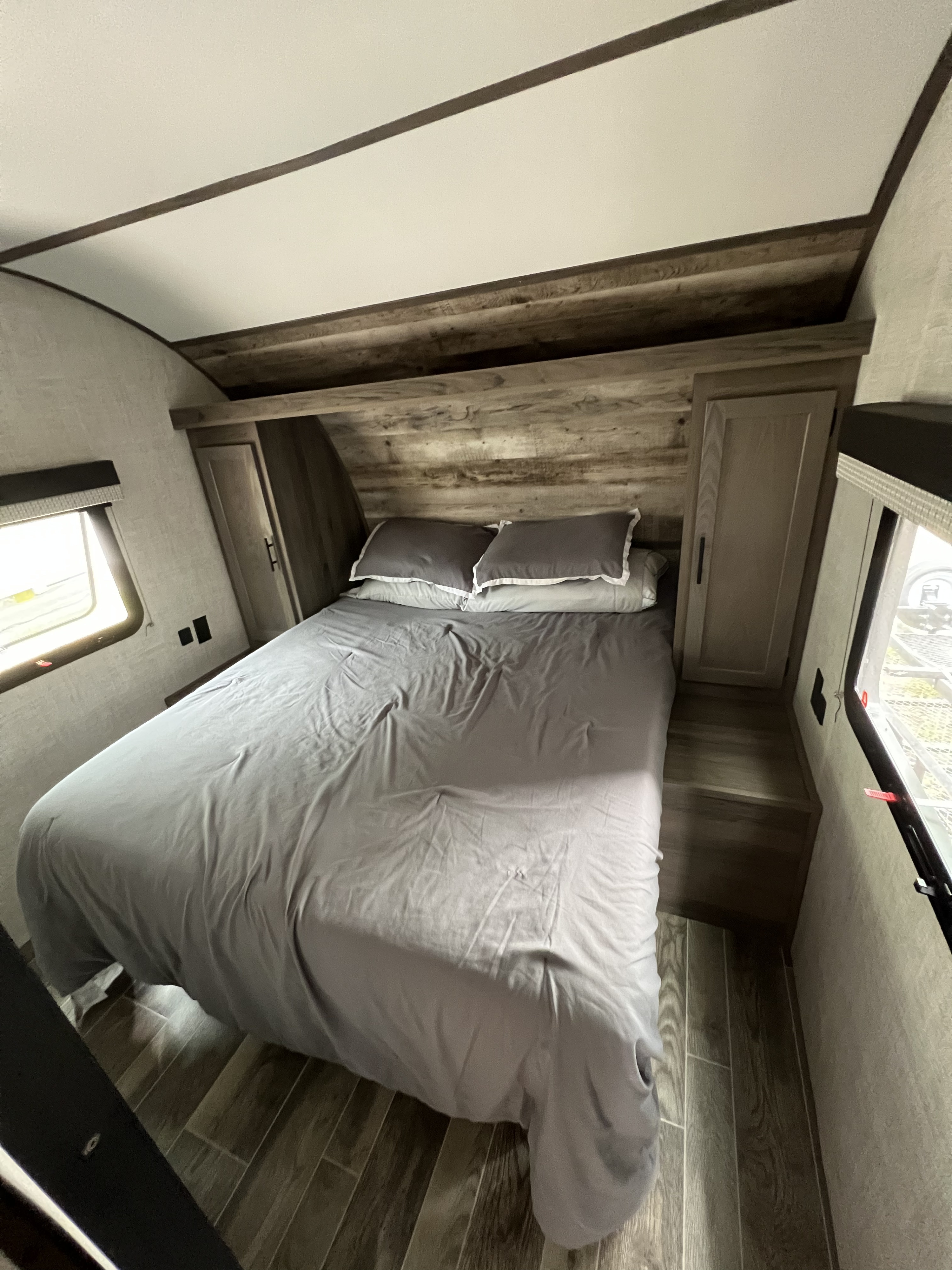This RV rental bedroom features a comfy bed, rustic wooden headboard, storage, and natural light.. Gulf Stream Ameri-Lite 2022