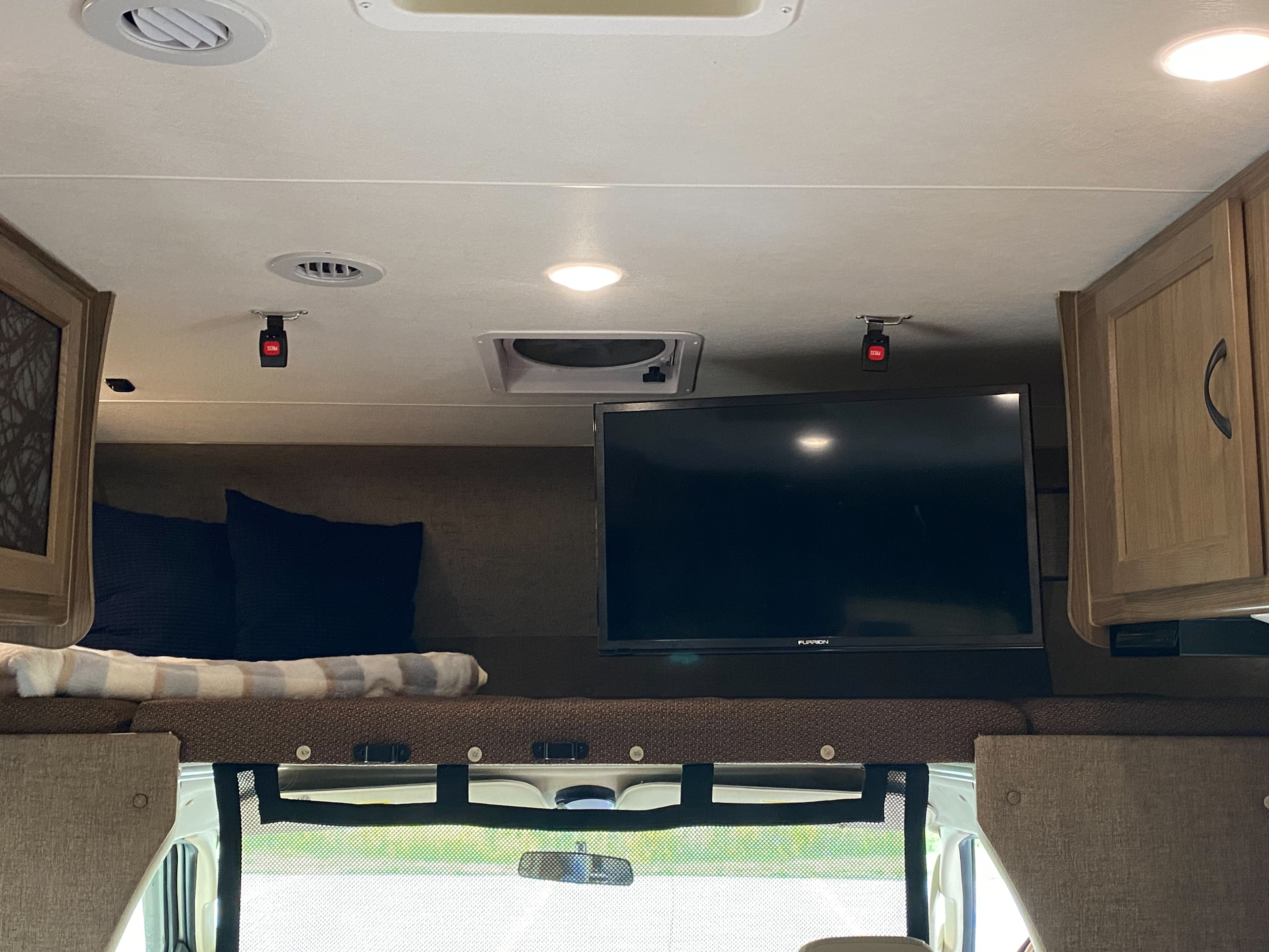 Inside an RV rental: a cozy overhead bunk with TV, lighting, and storage, overlooking the cab.. Forest River Coachmen Freelander 2017