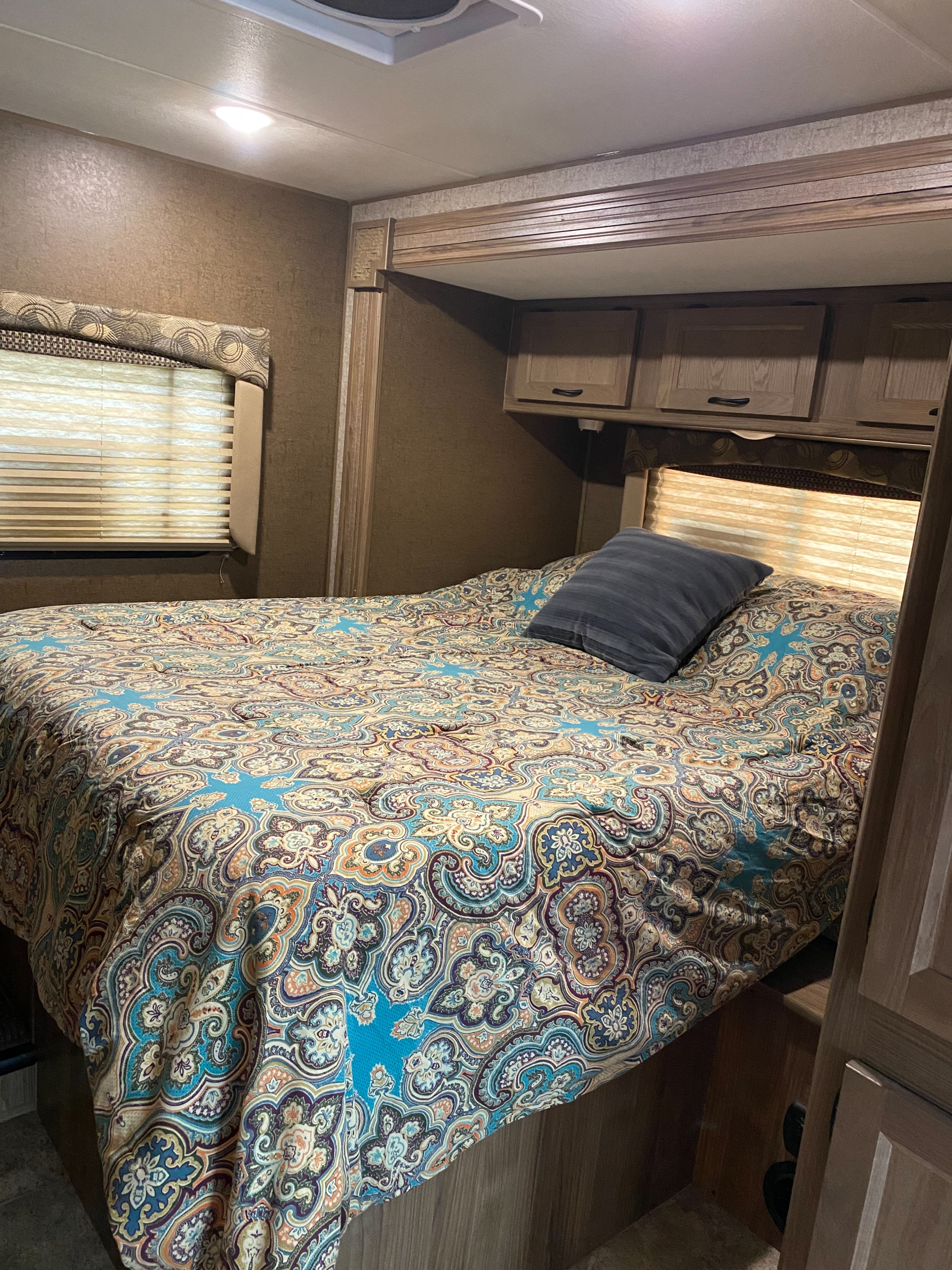 RV rental bedroom interior, featuring a bed with a colorful paisley comforter, overhead cabinets, and window blinds.. Forest River Coachmen Freelander 2017