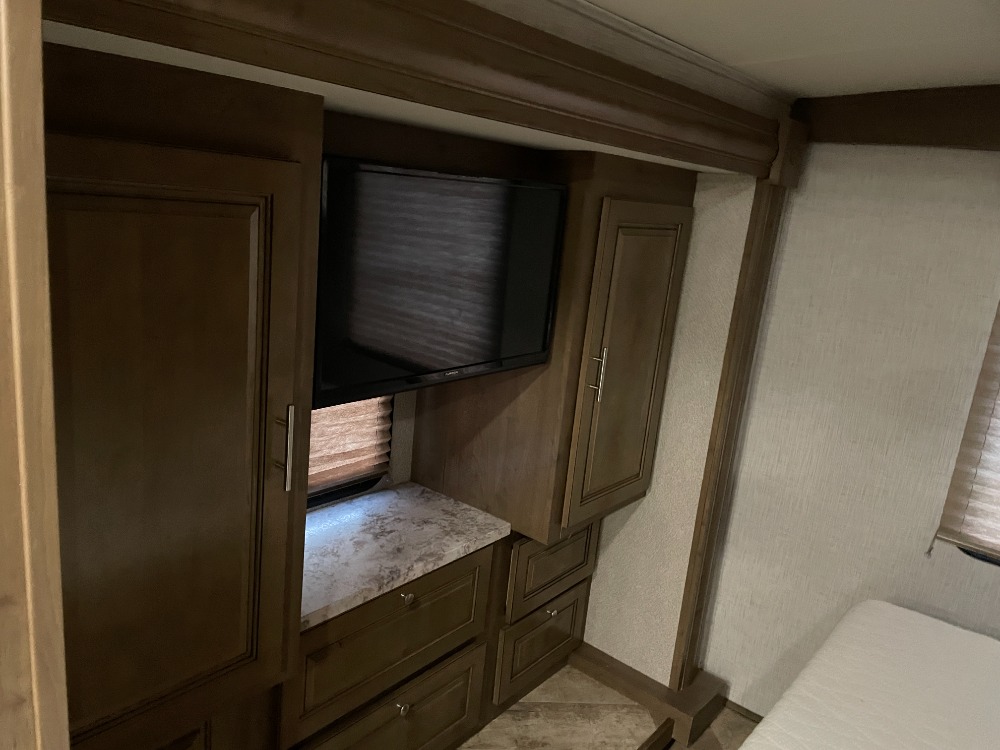 Explore this RV rental's bedroom: TV, built-in storage (cabinets/drawers), and a comfy bed area with window blinds.. Forest River Georgetown 3 Series 33b 2020