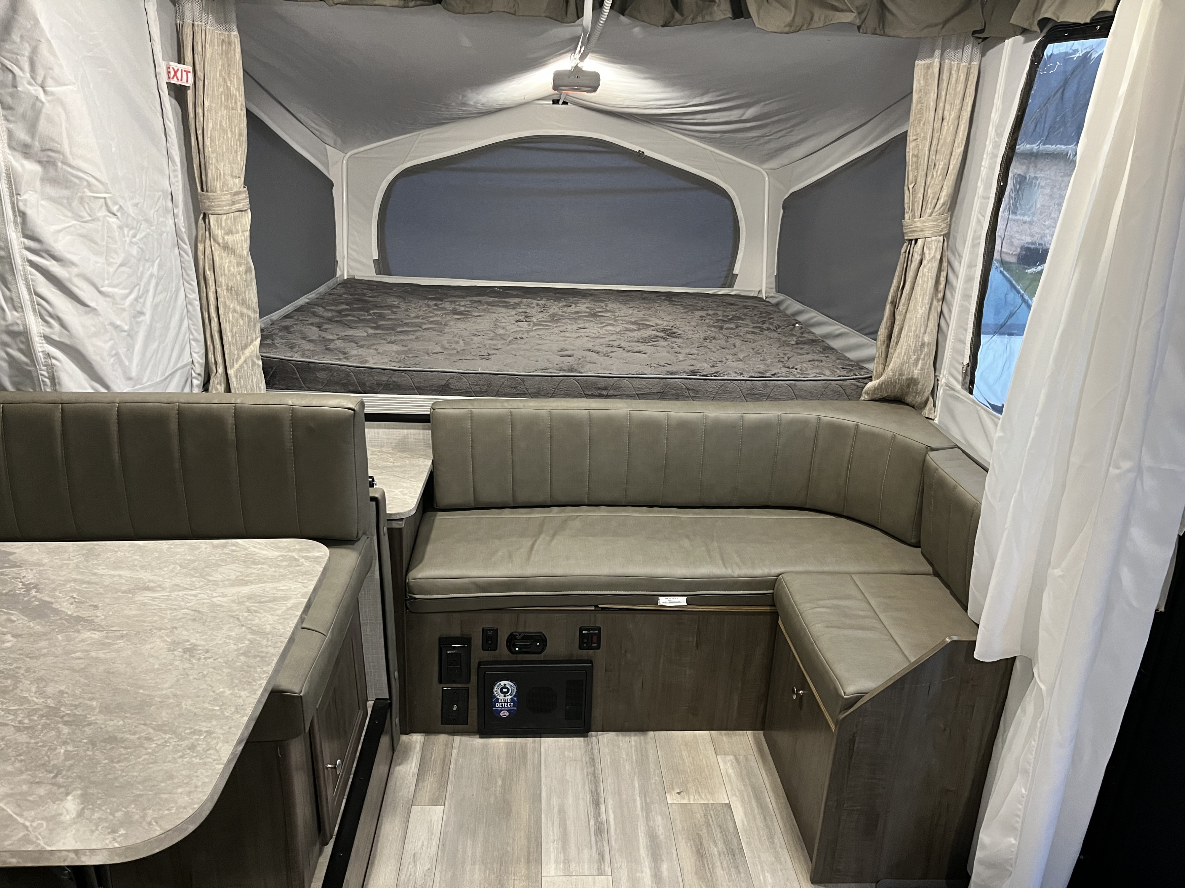 Bright interior of an RV rental pop-up camper, featuring a gray bed and U-shaped dinette with a utility panel.. Forest River Rockwood Freedom 2022