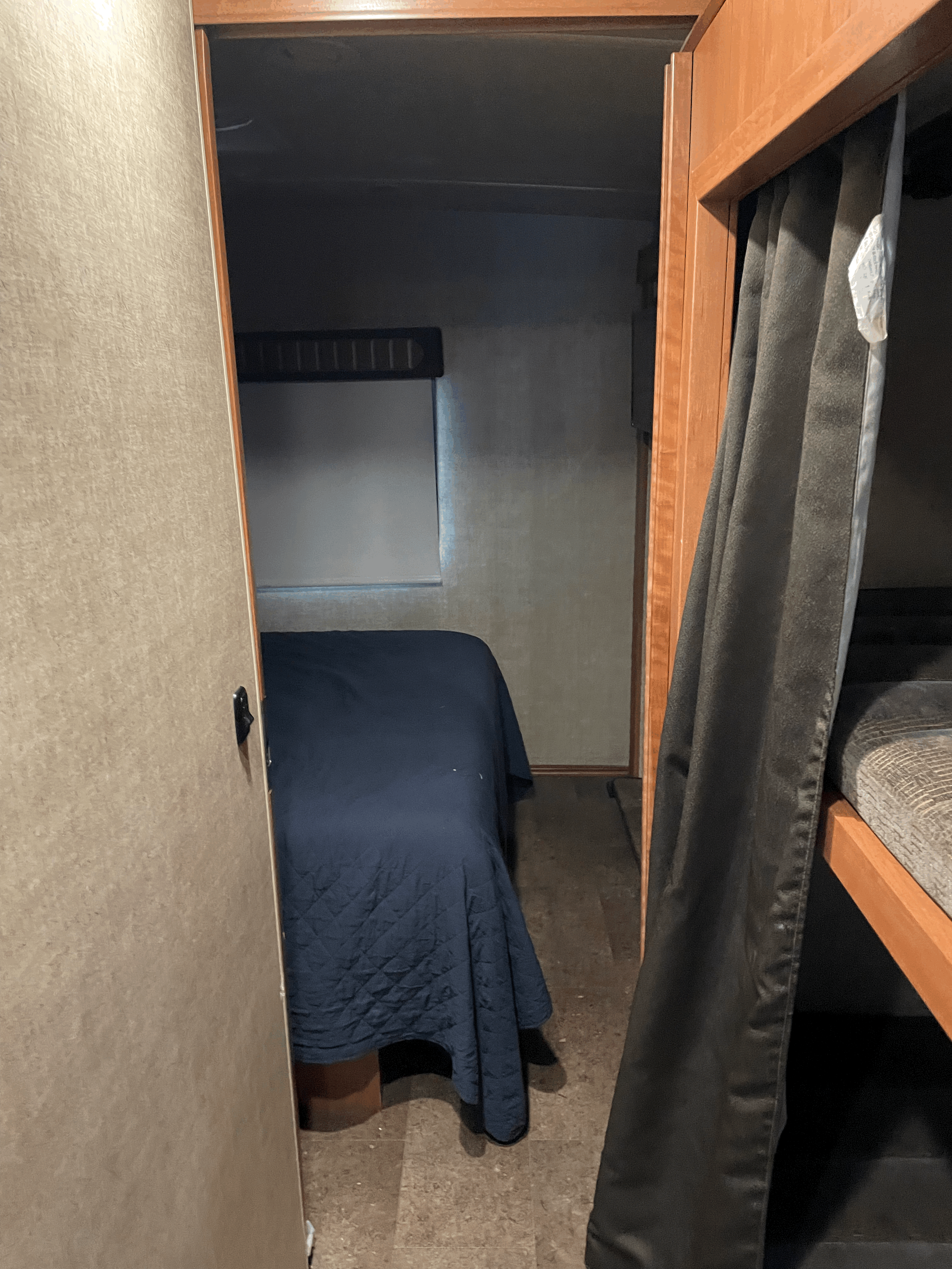 Cozy RV rental bedroom with a blue bed and window, adjacent to bunk beds hidden by dark curtains.. Winnebago Vista 2018