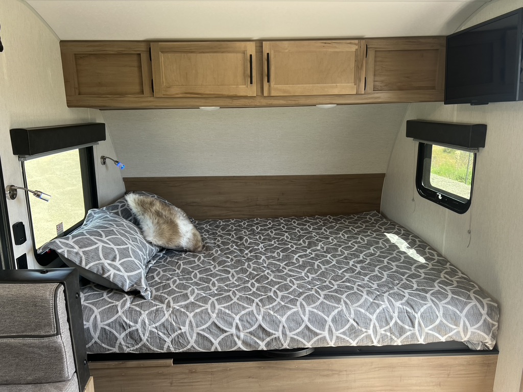 Experience comfort in this compact RV rental bedroom, featuring a patterned bed, wood cabinets, and two windows.. Forest River Cherokee Wolf Pup 17JGBL 2023