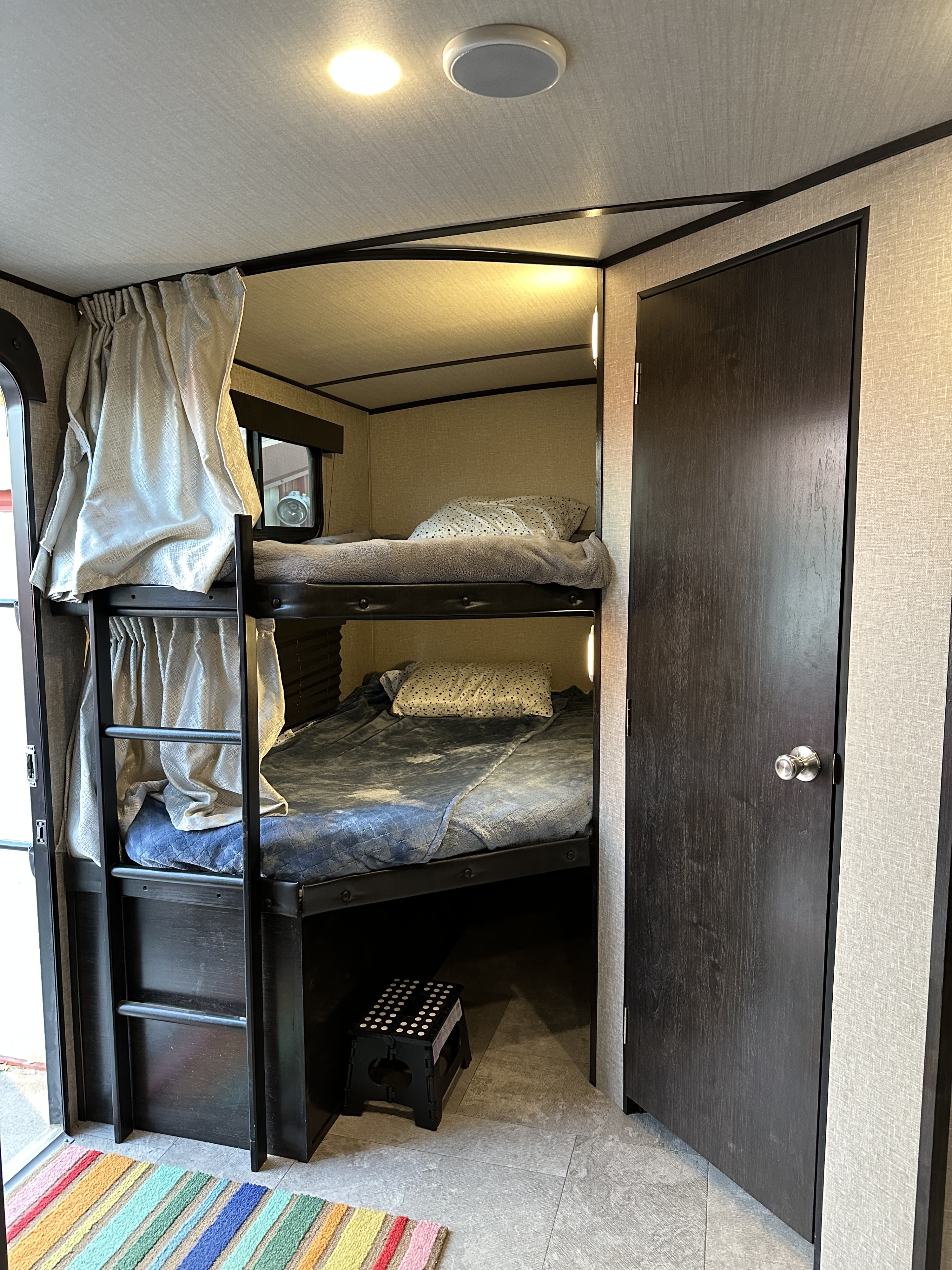 Cozy RV rental interior: stacked bunk beds with bedding, privacy curtains, and a dark door. Ideal compact sleeping area.. Grand Design Imagine 2020