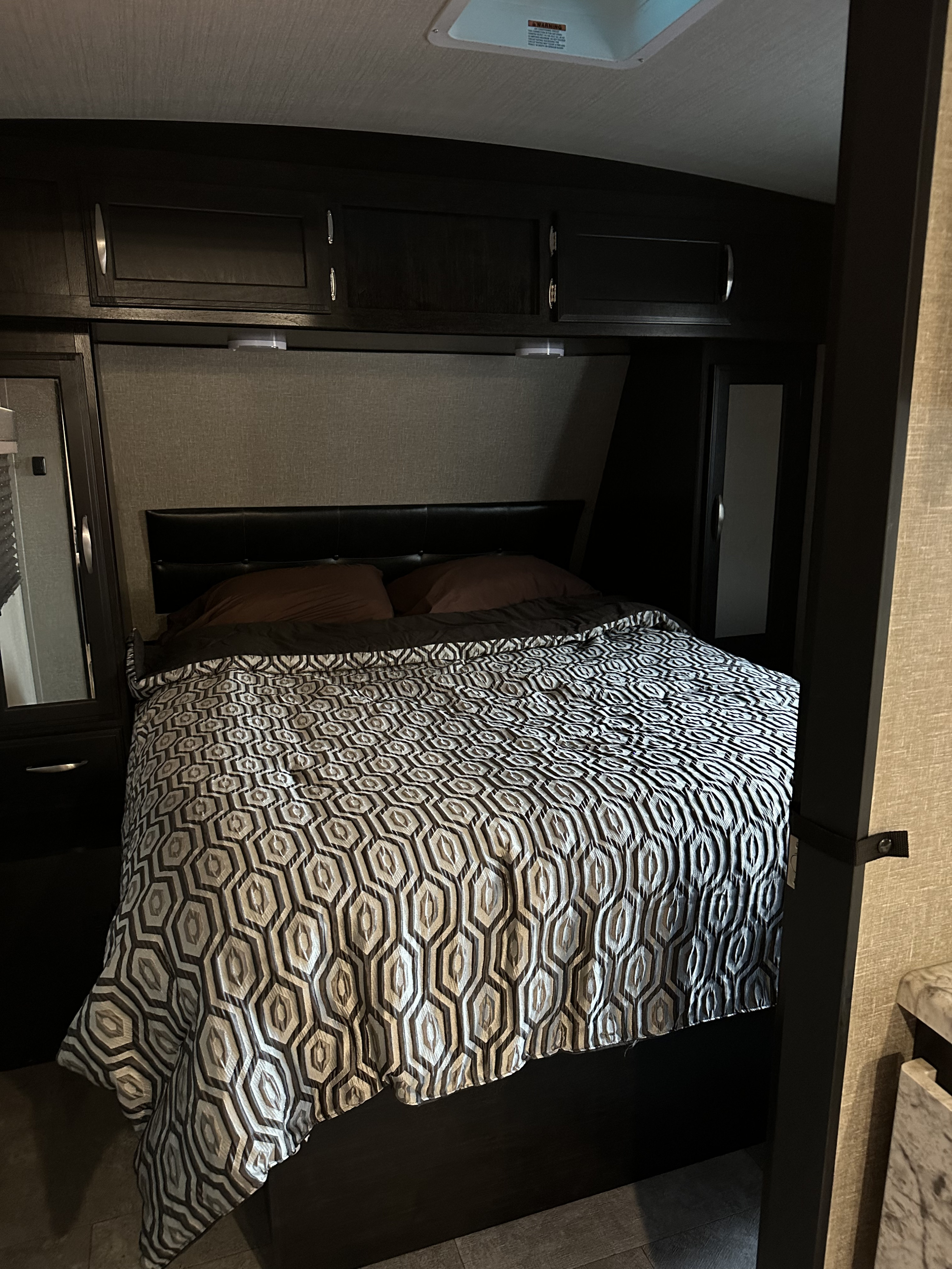 Cozy RV rental bedroom with dark wood built-in cabinets, a geometric patterned comforter, and compact design.. Grand Design Imagine 2020