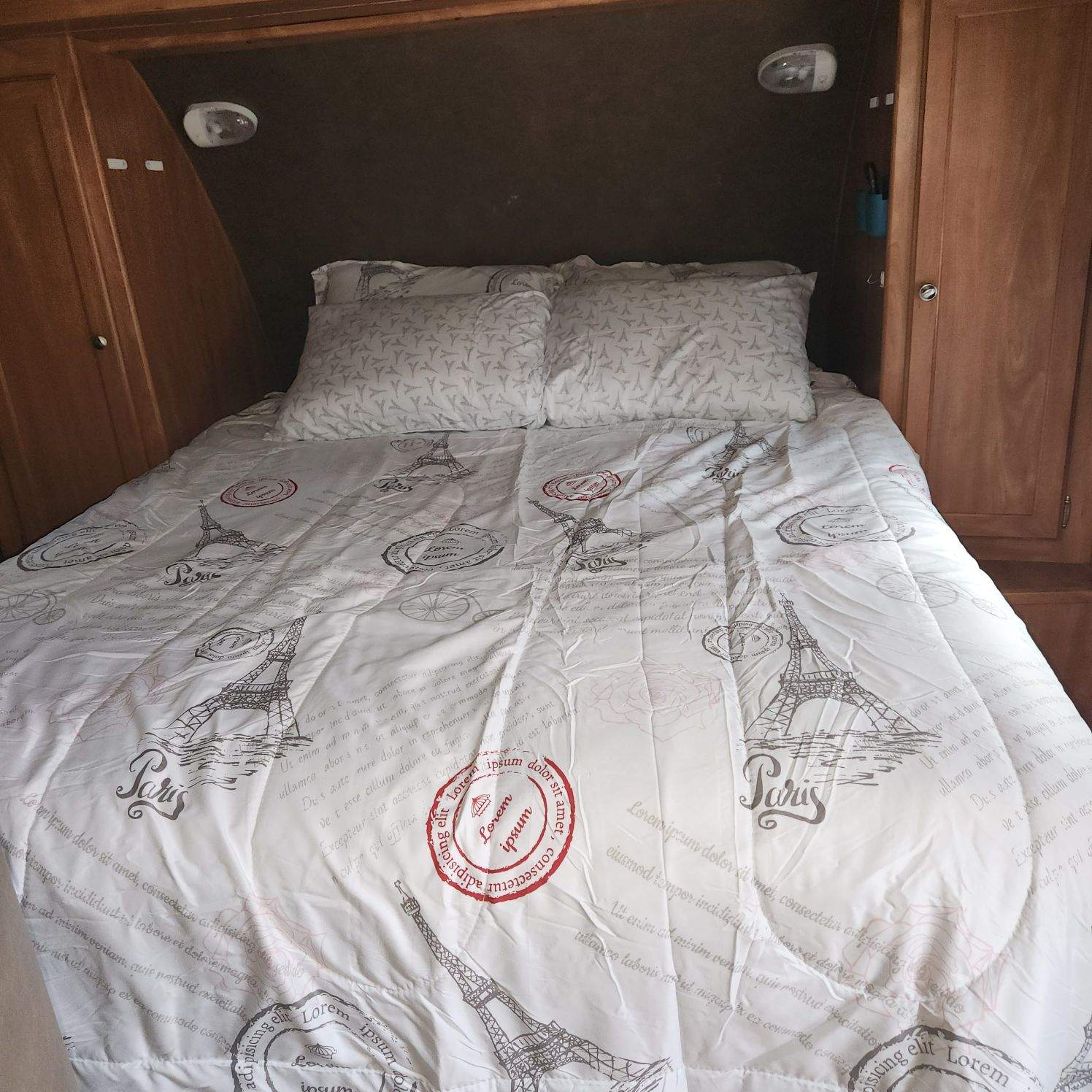 Cozy RV rental bedroom featuring a bed with a white and gray Paris-themed comforter and pillows, set in wood paneling.. Forest River Shasta Flyte 2015