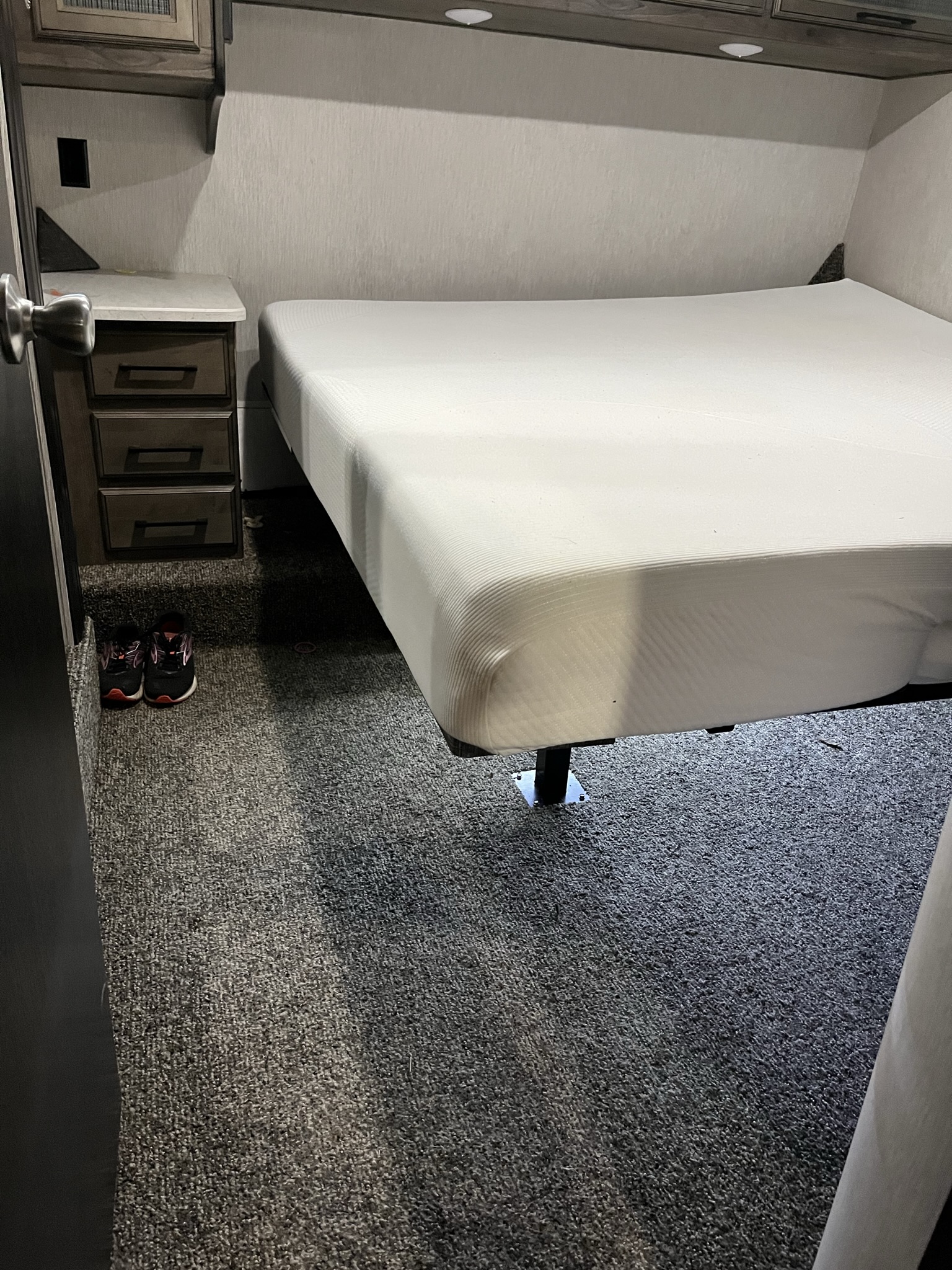 RV rental bedroom with a white bed, nightstand, and grey carpet. Sneakers rest on the floor.. Heartland Torque 2020