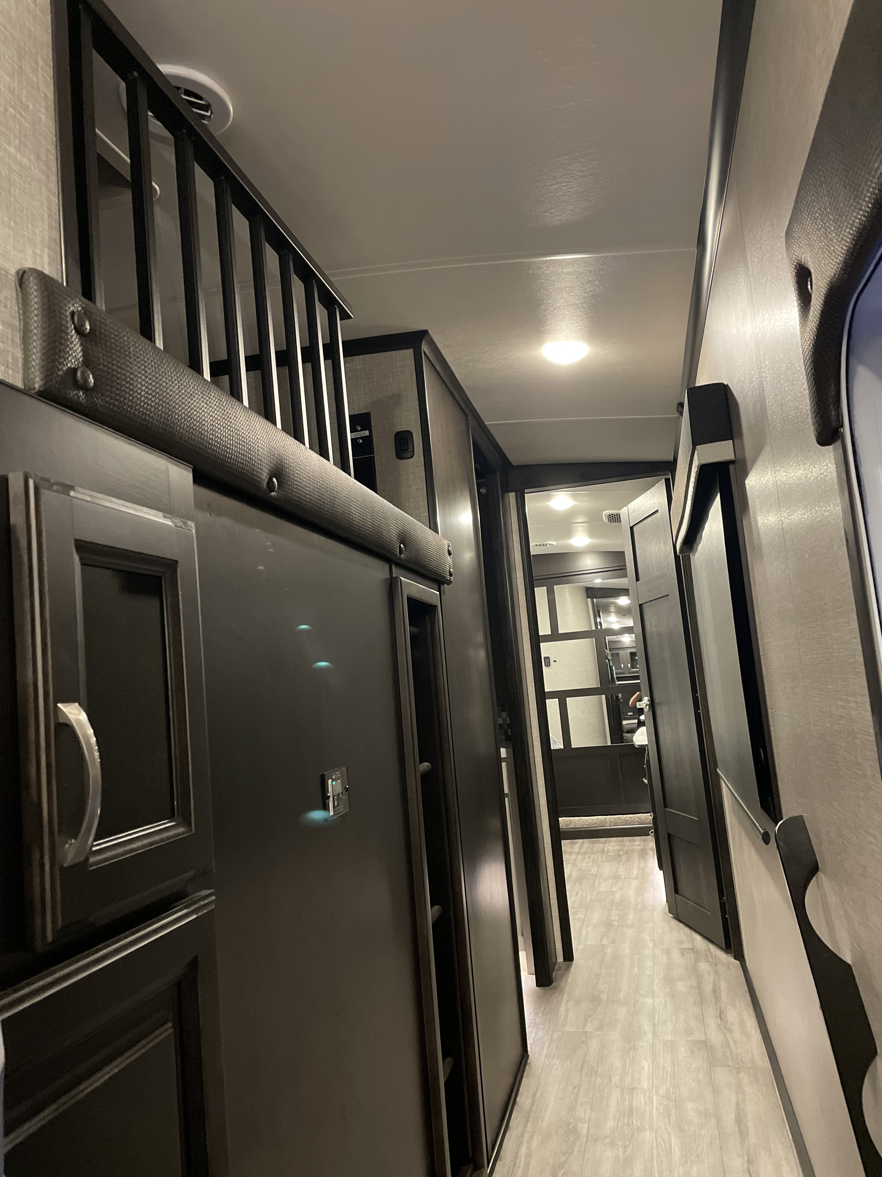 RV rental interior: Modern RV shows a sleek hallway with a cozy overhead loft, dark cabinetry, and inviting open doorways.. Jayco North Point 2022