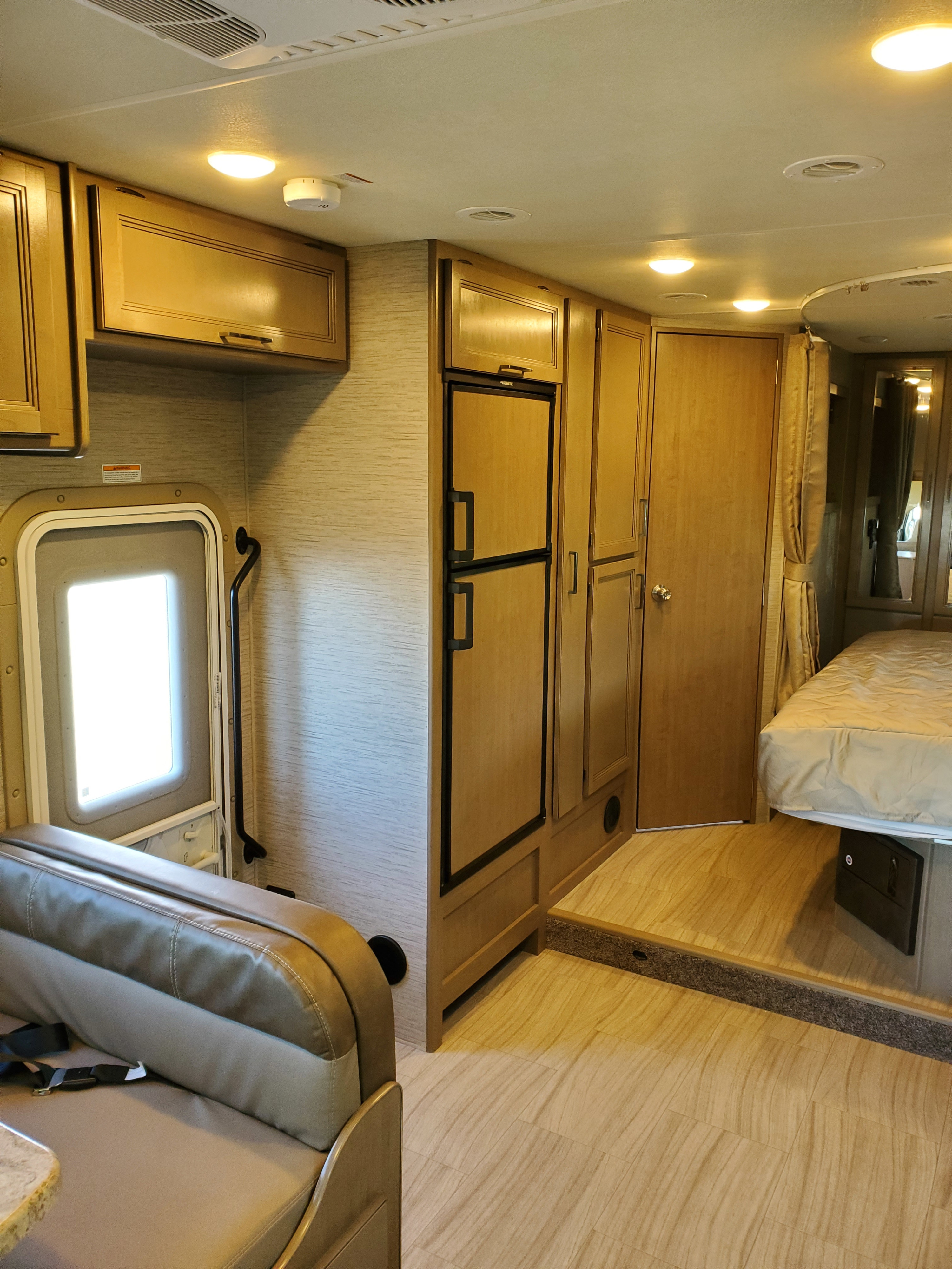 Inside this RV rental: a compact interior featuring kitchen, dinette, fridge, and a cozy bedroom with wood flooring.. Thor Motor Coach Daybreak 27DB 2021