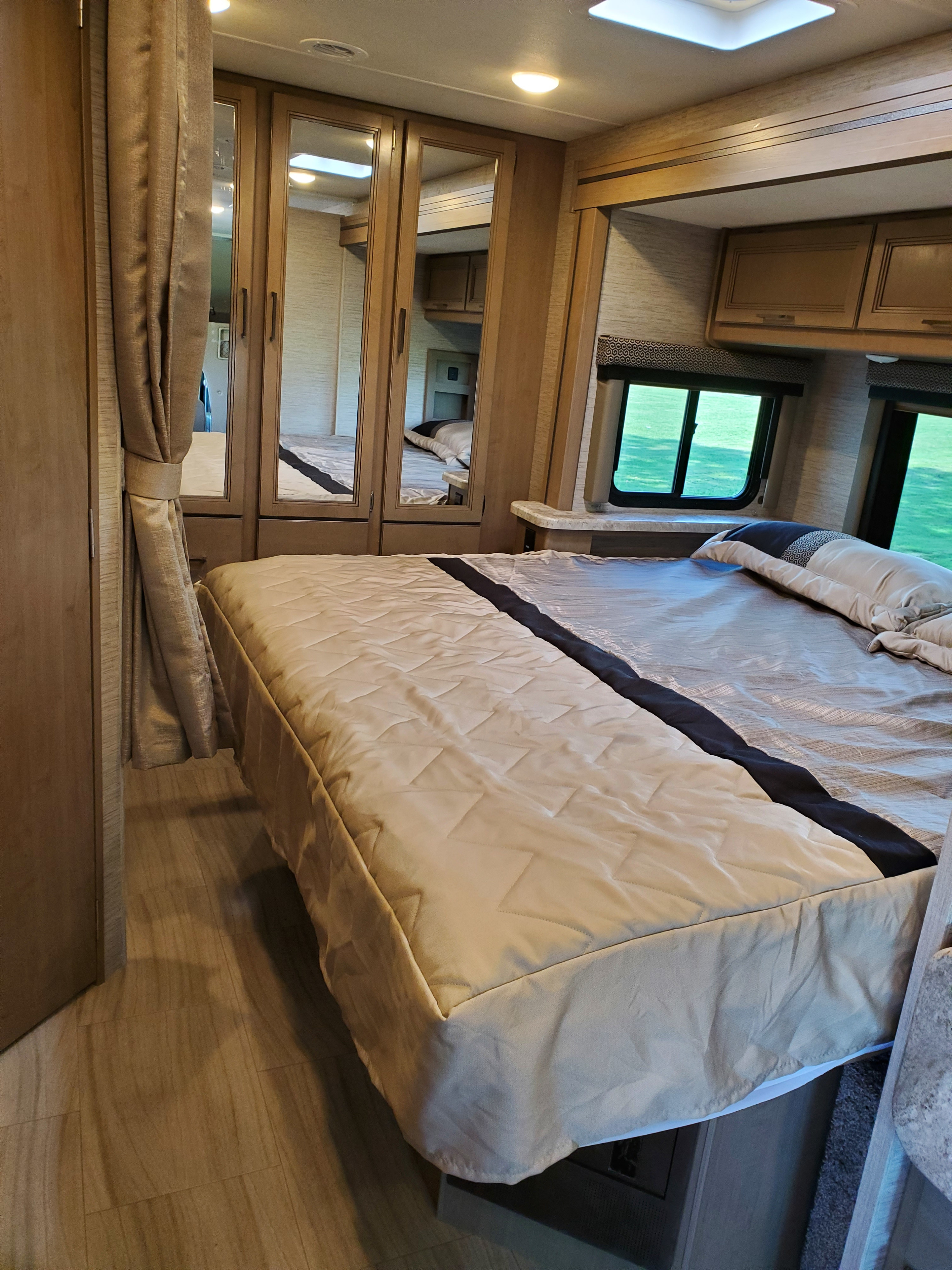 RV rental bedroom with a comfortable bed, mirrored closet, and windows showing green outdoor views.. Thor Motor Coach Daybreak 27DB 2021