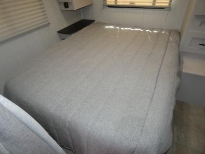 Inside this **RV rental**, a comfy bedroom features a large gray bed, an overhead shelf, and window blinds for privacy.. Coachmen Freelander 27QB 2023