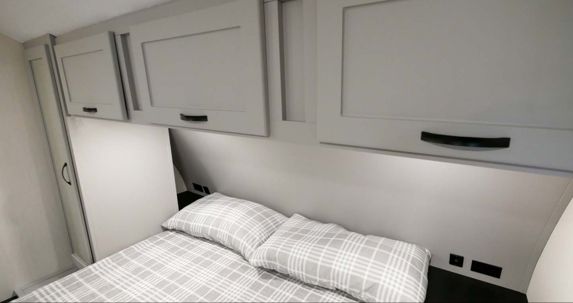 Compact RV rental bedroom with overhead cabinets, plaid bedding, and convenient outlets for a comfortable stay.. Forest River Vibe 2022