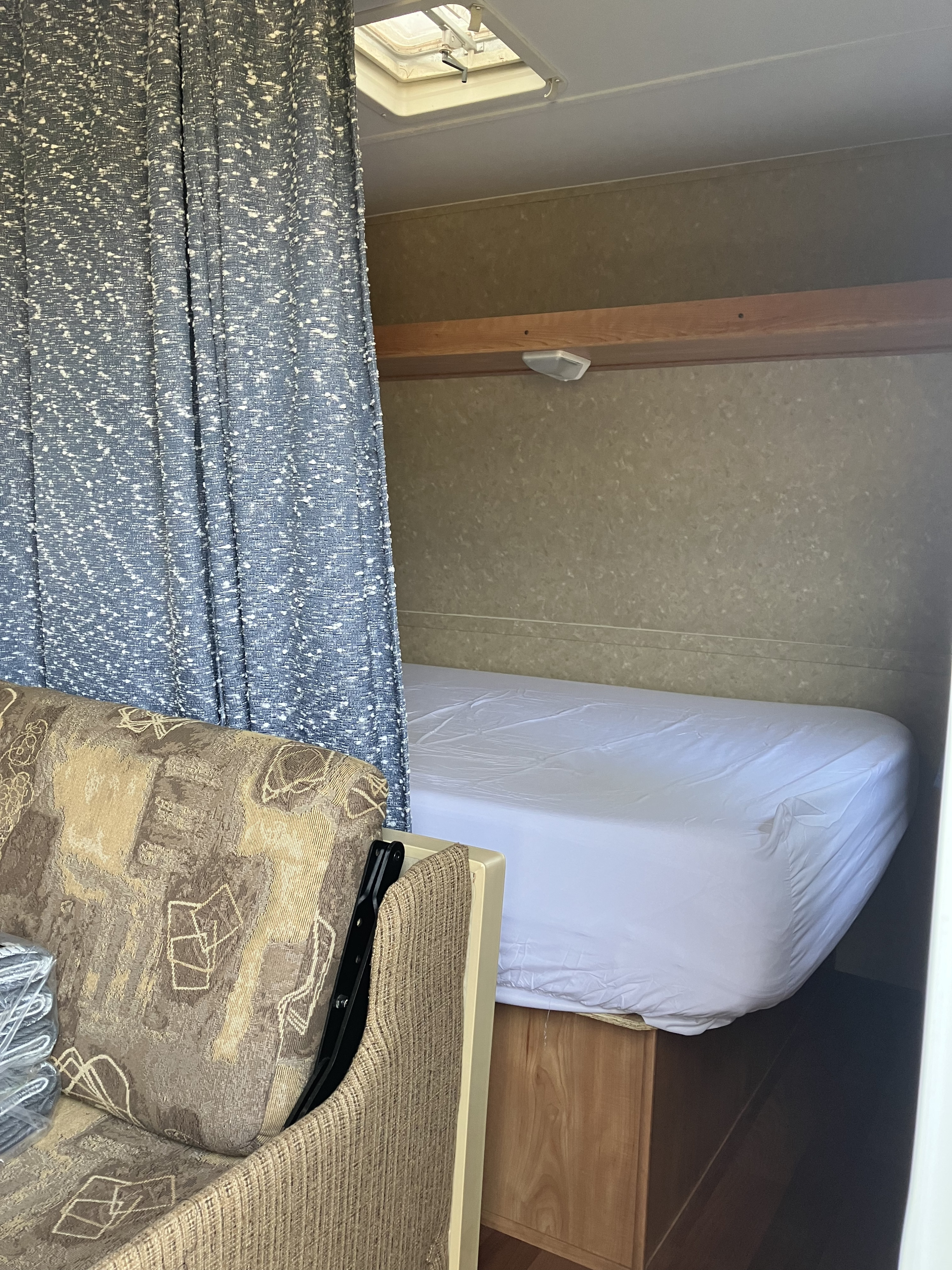Cozy RV rental interior featuring a bed with white sheets, a privacy curtain, and a patterned couch, ideal for travel.. Gulf Stream Ameri-Lite 25 BS 2008
