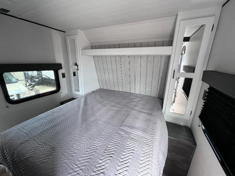 Cozy RV rental bedroom with a large bed, wood panel headboard, window, and mirrored cabinet. Ideal for travel.. Keystone RV Hideout 2023