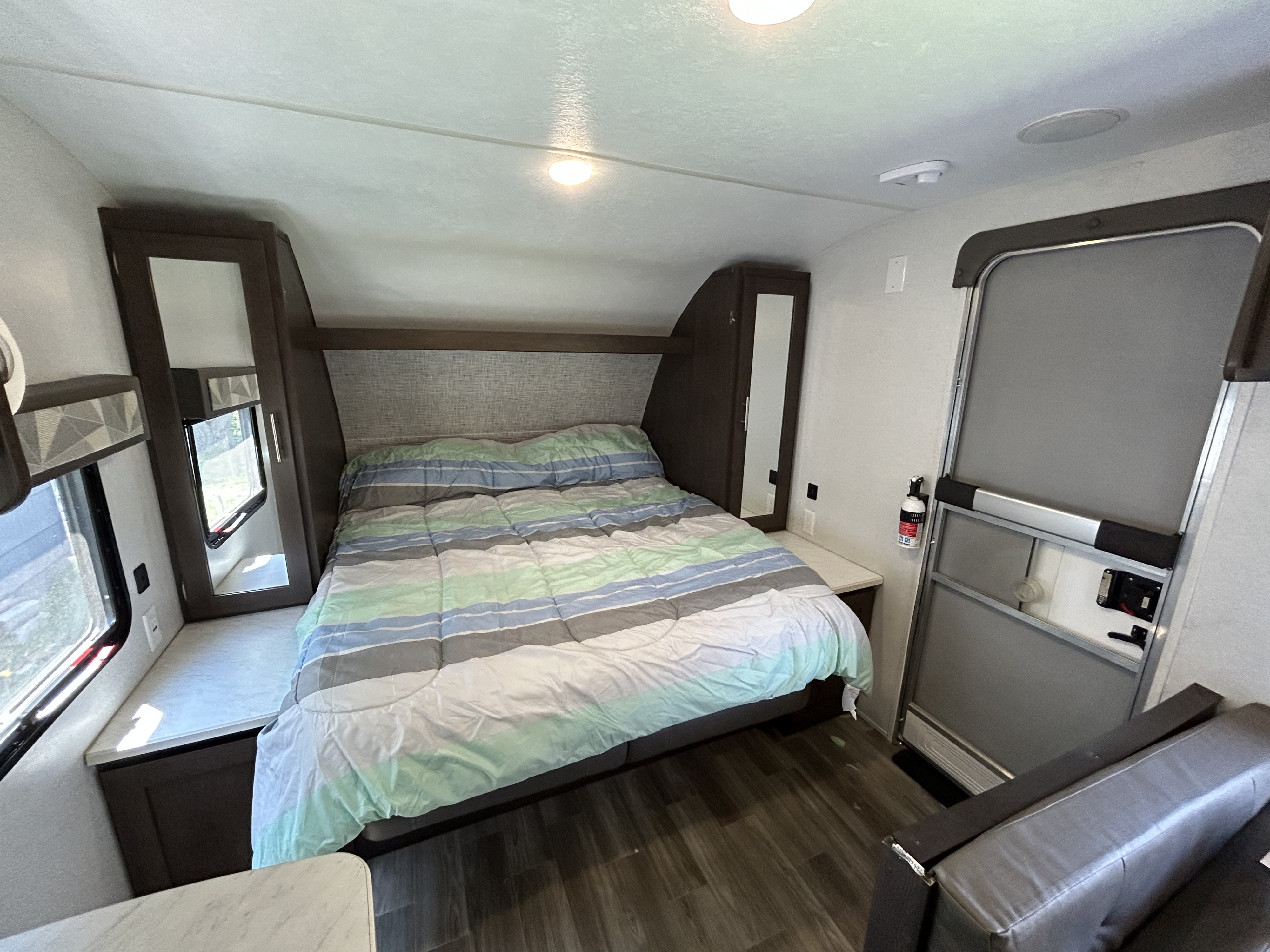 Cozy RV rental bedroom features a striped bed, built-in storage, and essentials like a fire extinguisher.. Forest River Salem Cruise Lite 2019