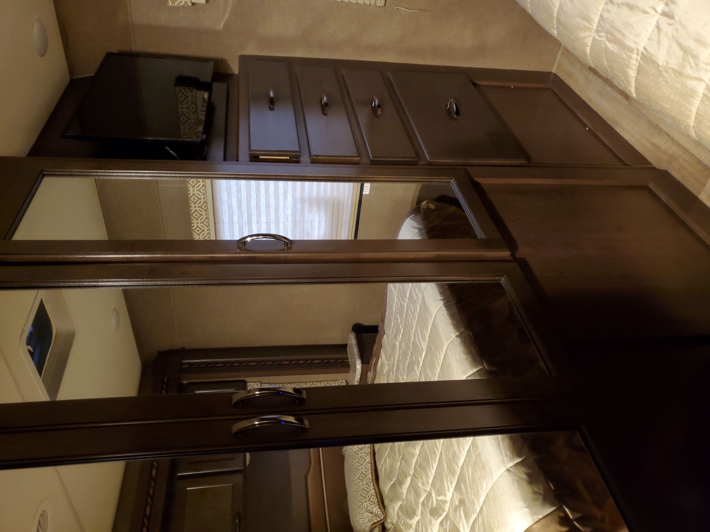 This RV rental's cozy bedroom features a TV, dark wood cabinets, and mirrored closet doors reflecting the bed.. Thor Freedom Elite 2018