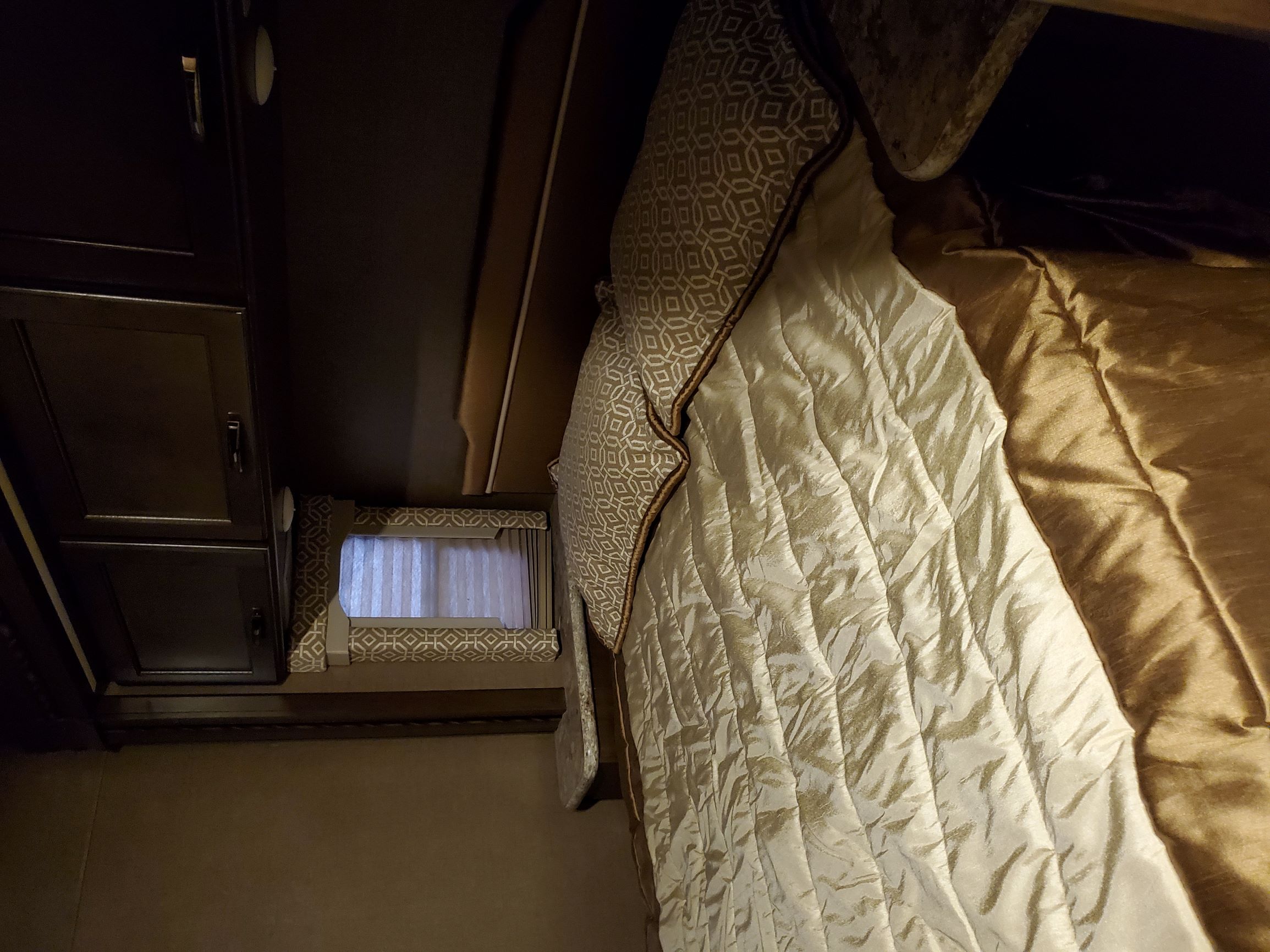 Cozy RV rental bedroom with patterned bed linens, dark cabinets, and a window, offering a compact sleeping area.. Thor Freedom Elite 2018