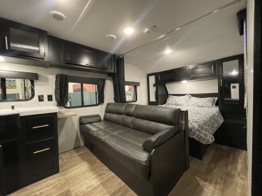 Spacious RV rental interior featuring a comfy bed, convertible sofa, and sleek dark cabinetry. Perfect for your next adventure!. Forest River Cherokee Grey Wolf Special Edition 2022