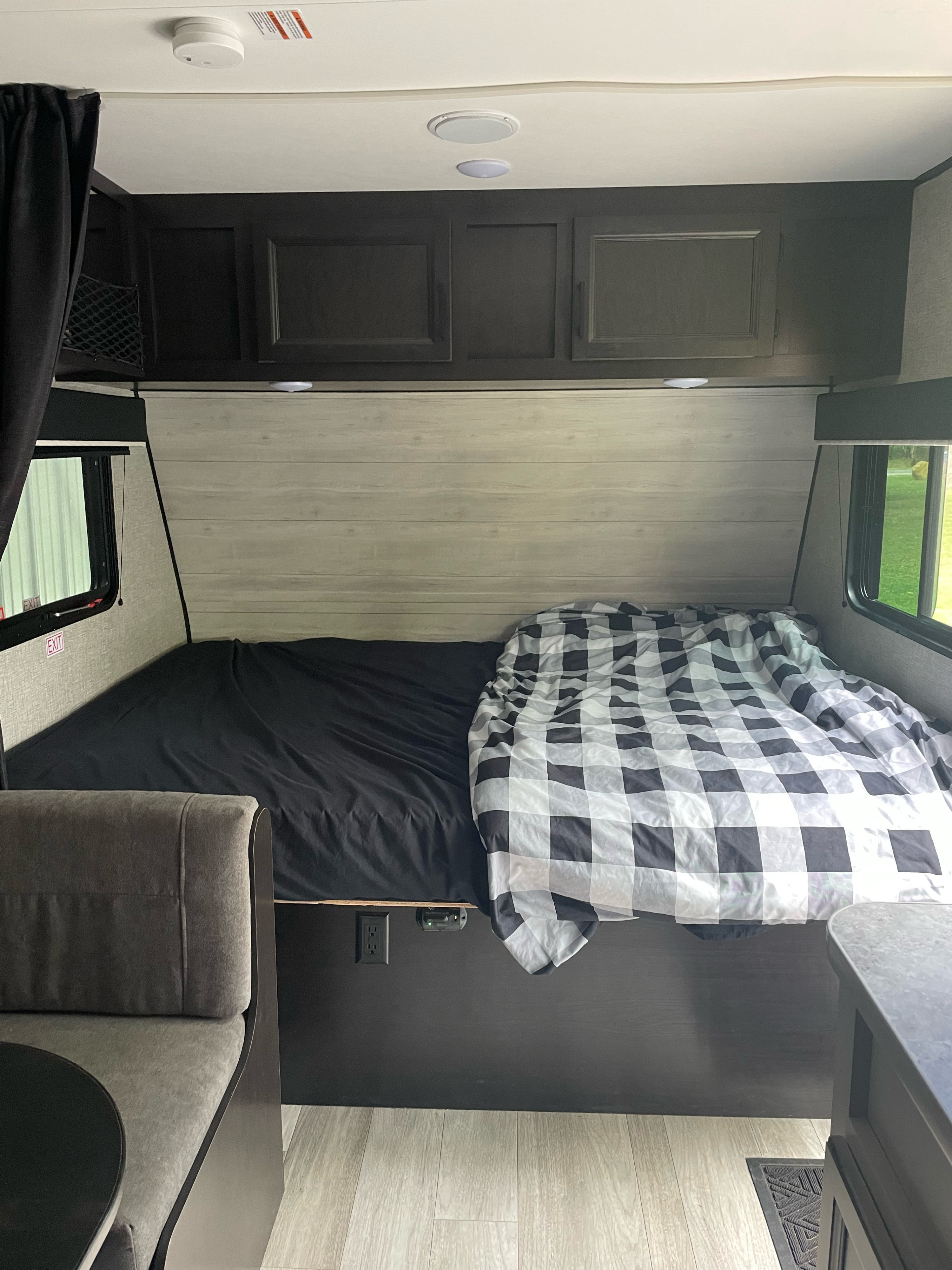Inside an **rv rental**: a cozy bed with a buffalo check comforter, light wood paneling, and dinette seating.. Jayco Jay Flight SLX 2022