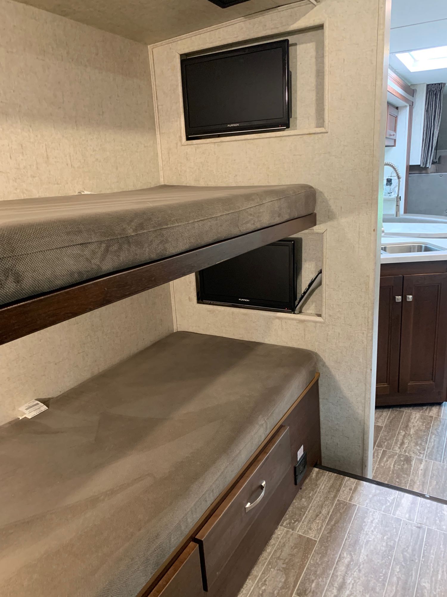 Cozy RV rental interior: gray bunk beds each with a TV, plus a kitchen with sink and dark wood cabinets.. Forest River Sunseeker 2018
