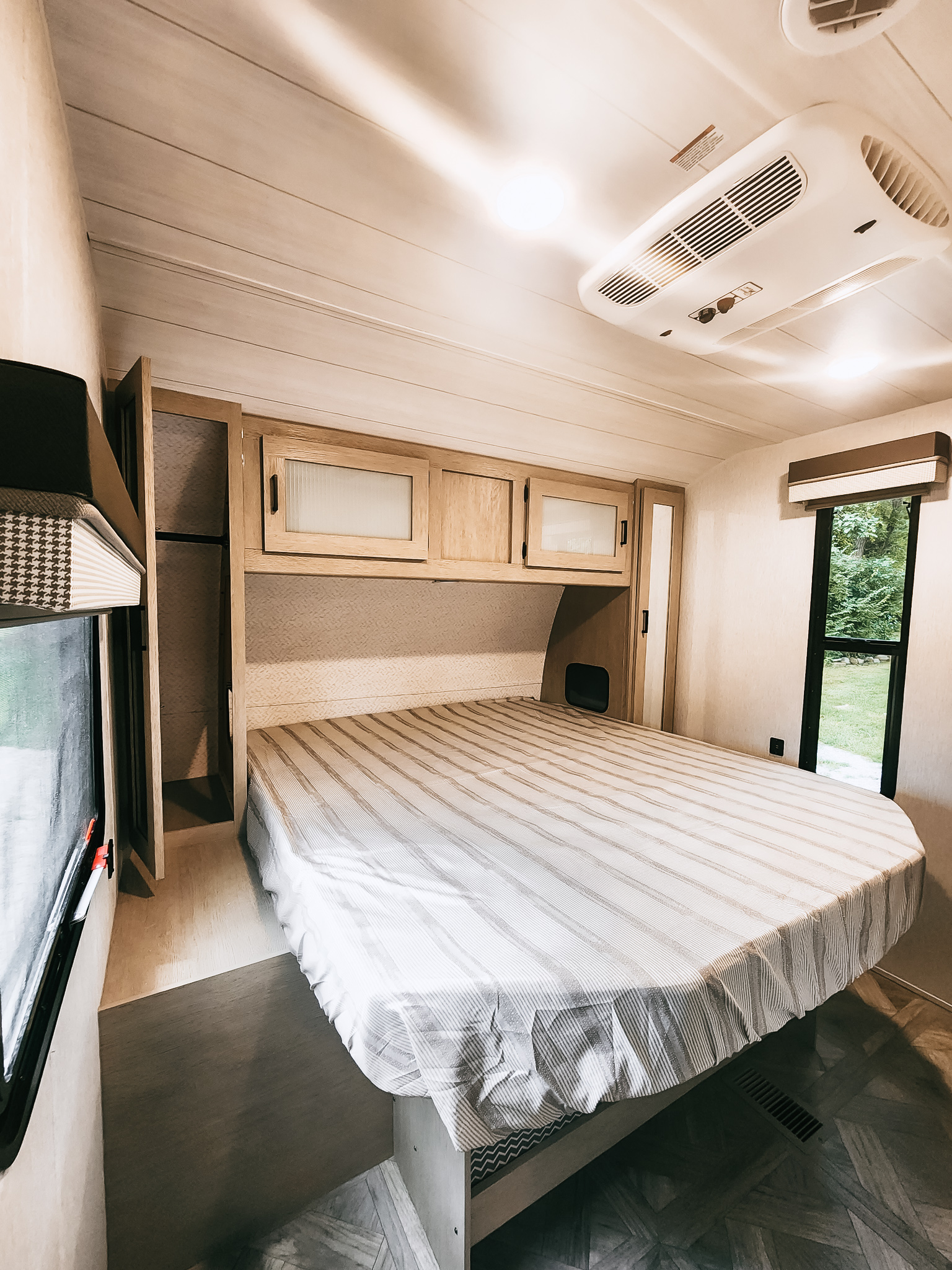 RV rental bedroom: a cozy, bright space with a striped bed, overhead cabinets, closet, and AC for your travels.. Forest River Wildwood 2023