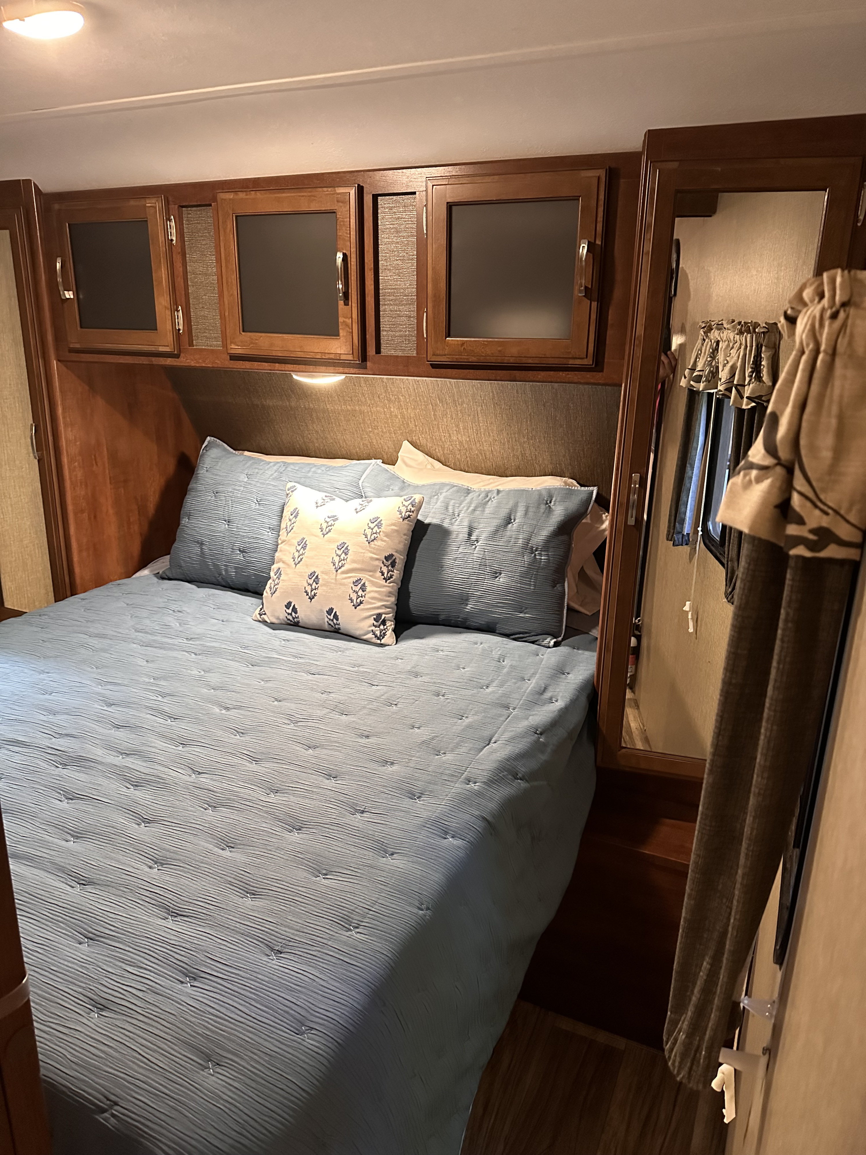 RV rental bedroom with a light blue quilted bed, overhead cabinets, and a mirror.. Keystone RV Passport Grand Touring 2016
