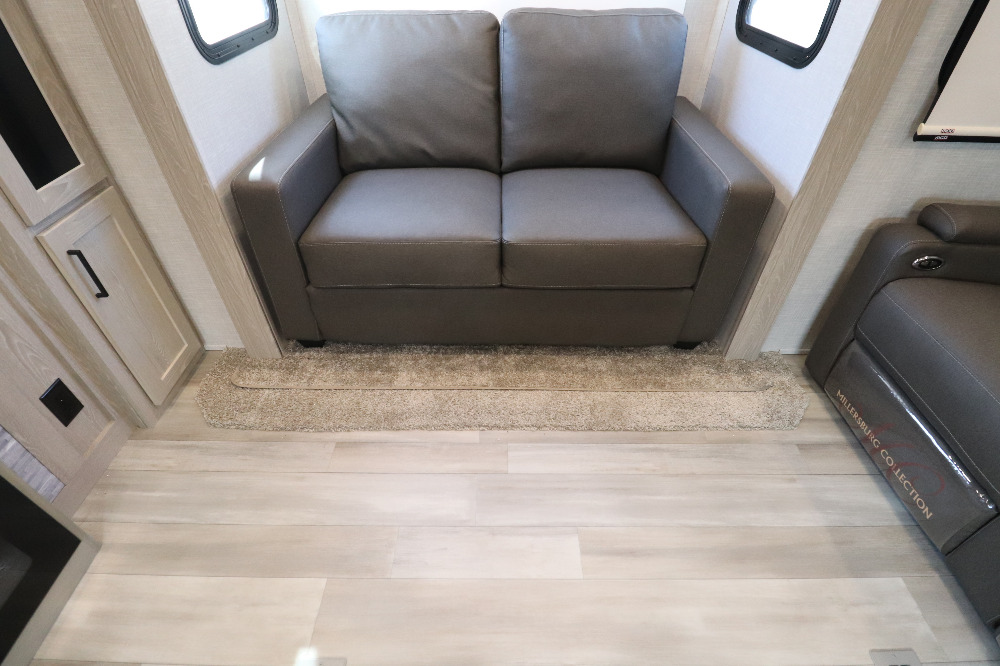 Inside this modern **RV rental**, find a comfortable gray loveseat, light wood flooring, and cabinetry, offering a homey travel experience.. Forest River Rockwood Signature Ultra 2021