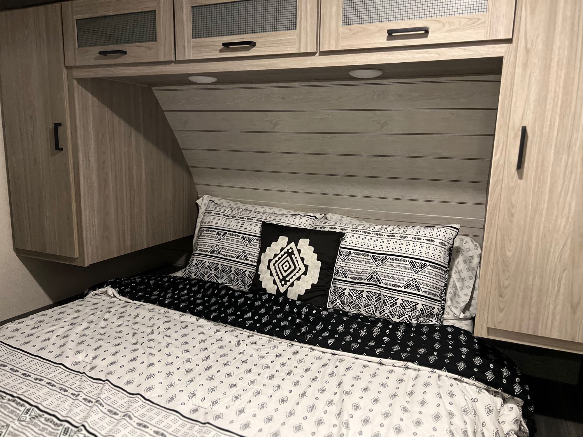 Cozy RV rental bedroom with modern light wood cabinetry, under-cabinet lighting, and stylish black/white geometric bedding.. Keystone RV Passport GT 2022