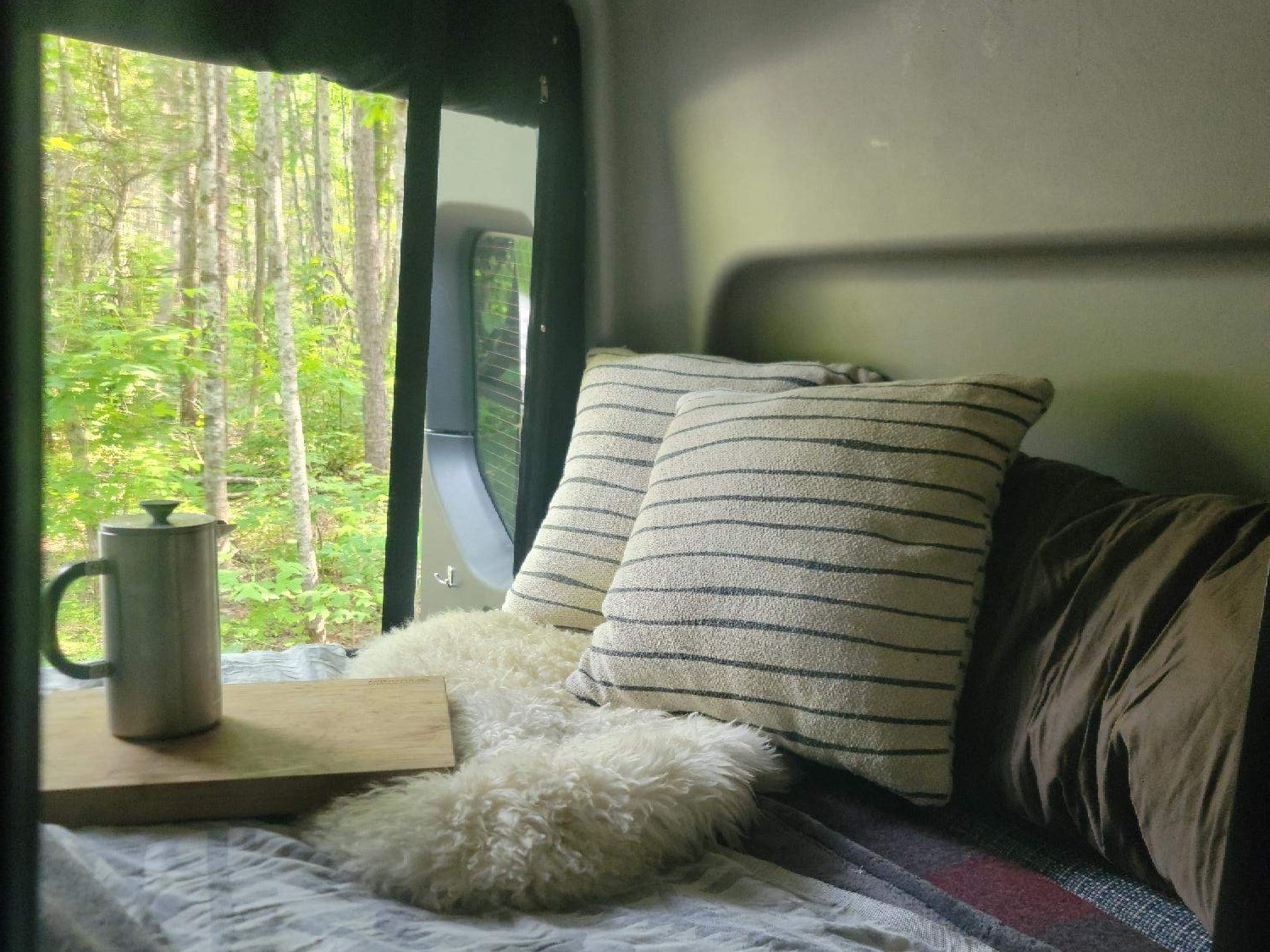 Cozy rv rental bedroom scene with forest views, a coffee setup, and plush pillows. Your peaceful escape awaits.. Winnebago Revel 2022