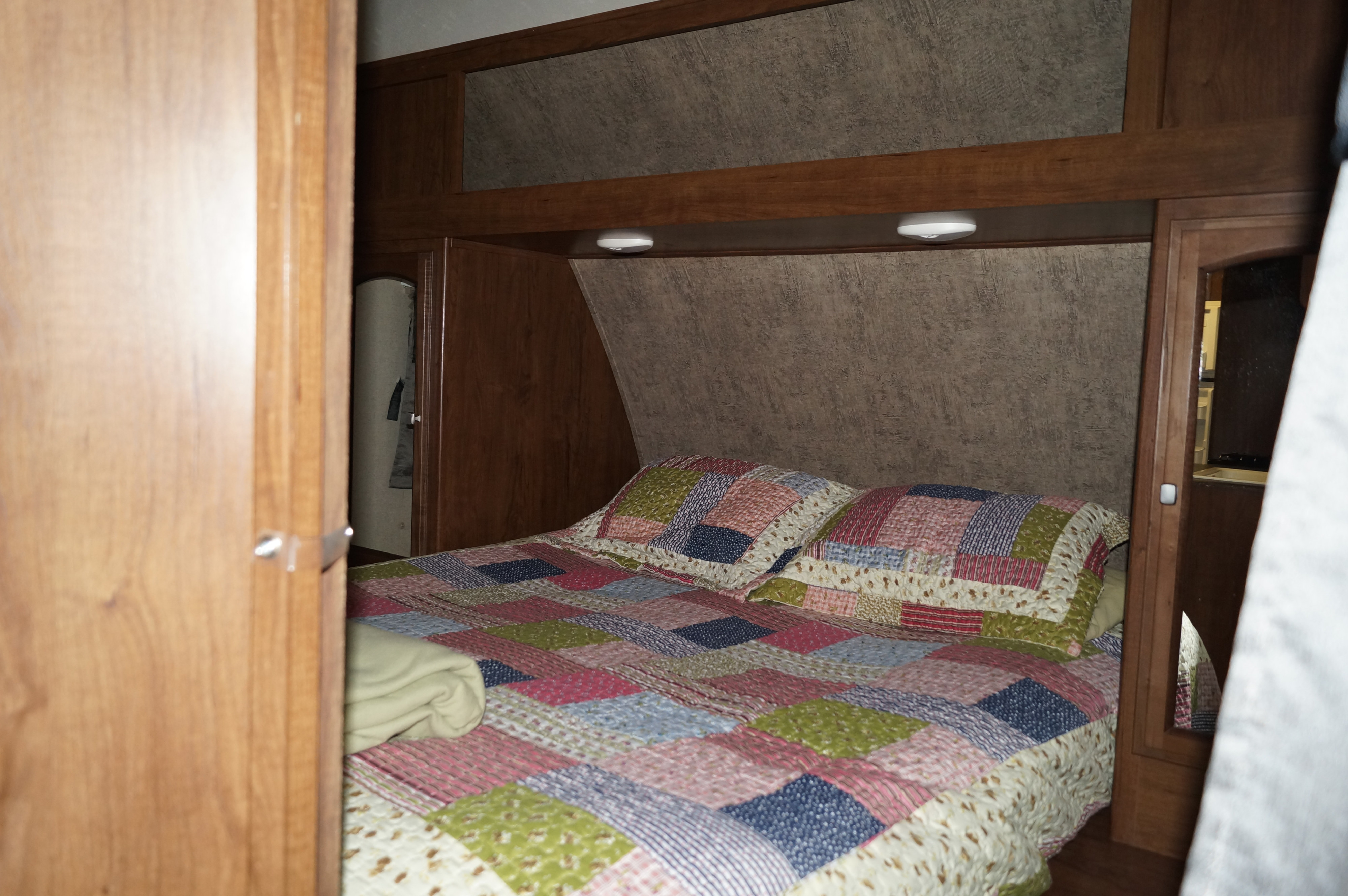 An RV rental's cozy bedroom, showcasing a colorful patchwork quilt on the bed with overhead storage and lighting.. Coachmen Freedom Express 2020