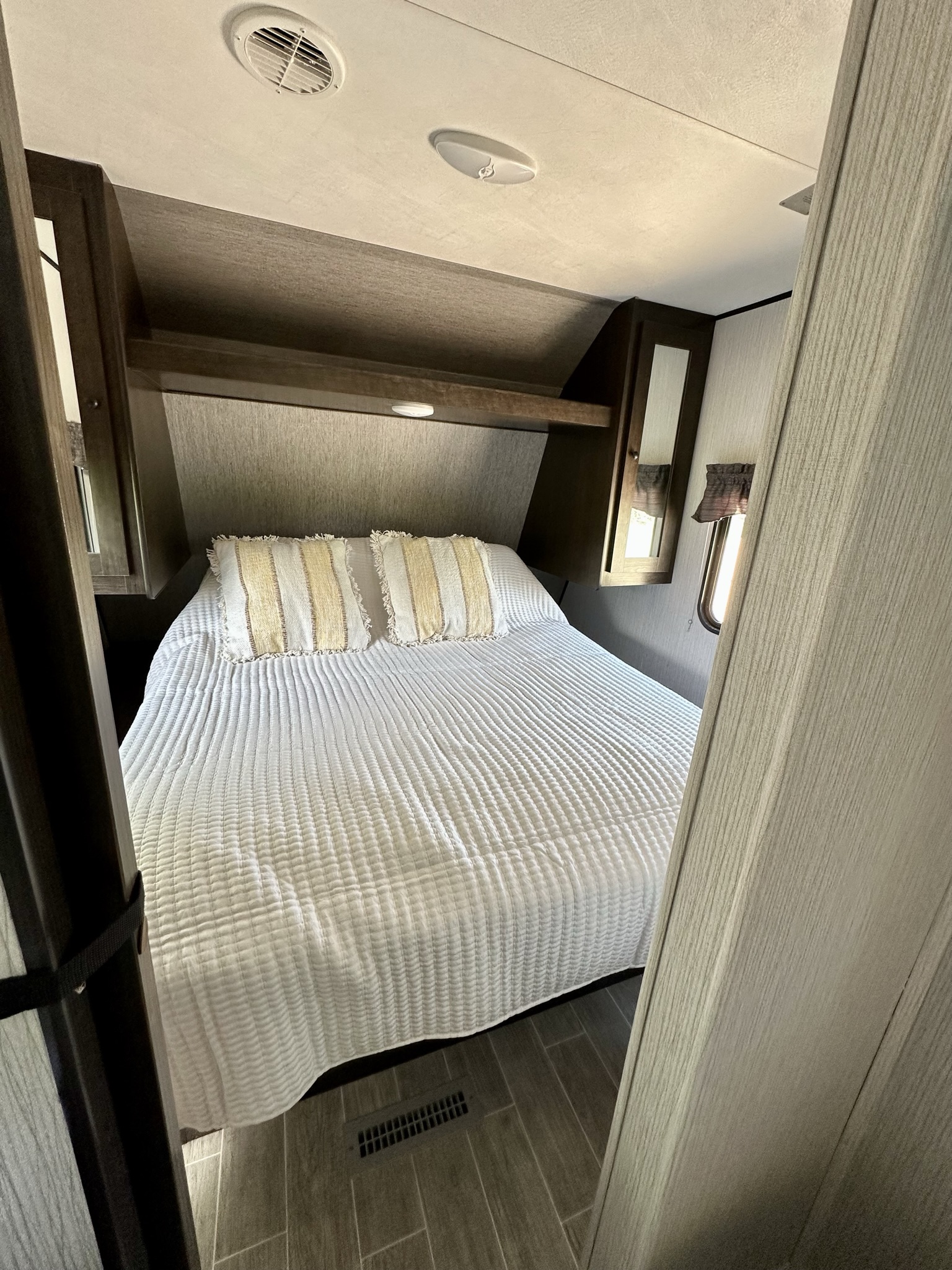 Cozy RV rental bedroom with a large bed, white textured bedding, wood cabinetry, and tiled floor.. Heartland RVs Trail Runner 2021