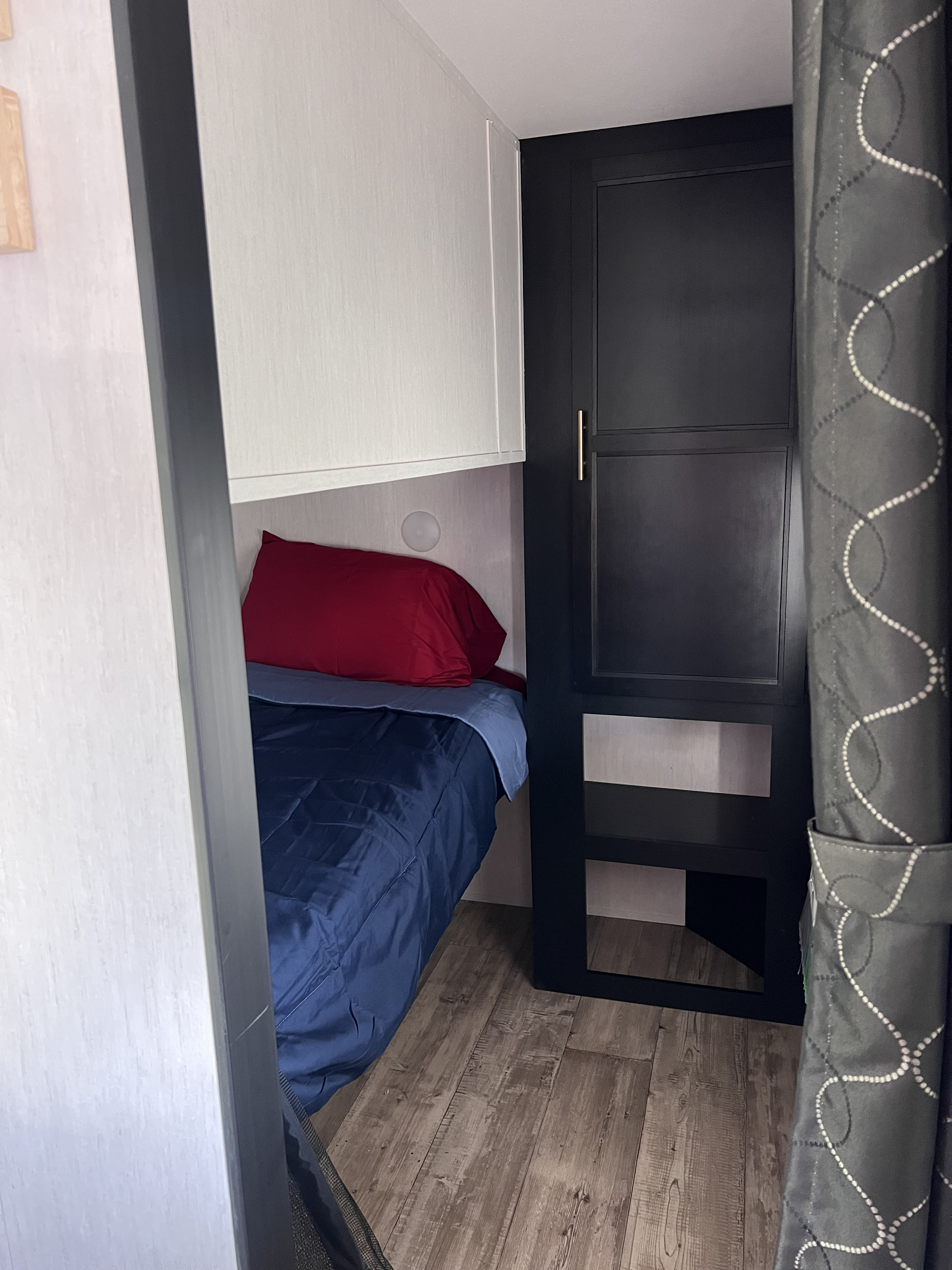 Compact RV rental sleeping area with a bunk bed, red pillow, blue comforter, and dark built-in storage. Features wood-look flooring.. Forest River Cherokee 2022