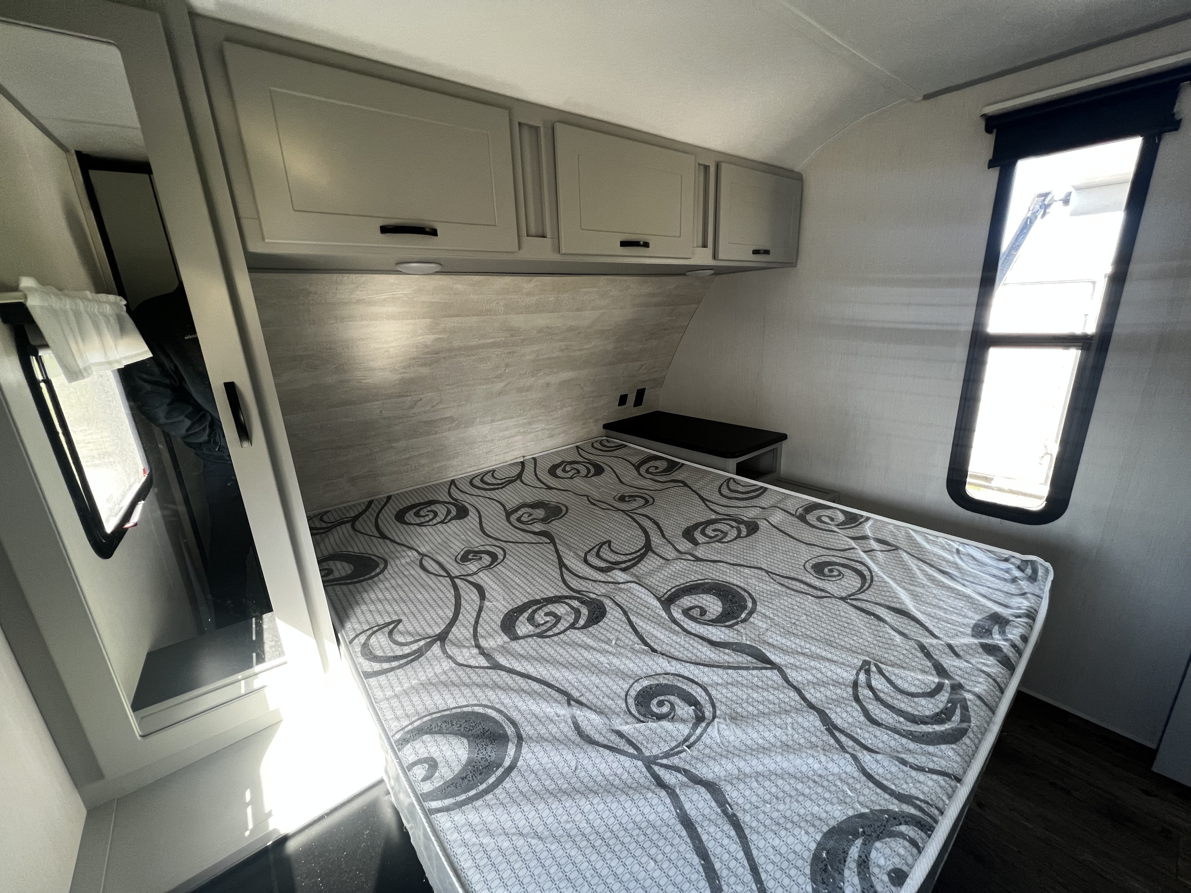 Inside a modern RV rental bedroom, featuring a patterned mattress, overhead cabinets, and natural light from windows.. Forest River Vibe 2022