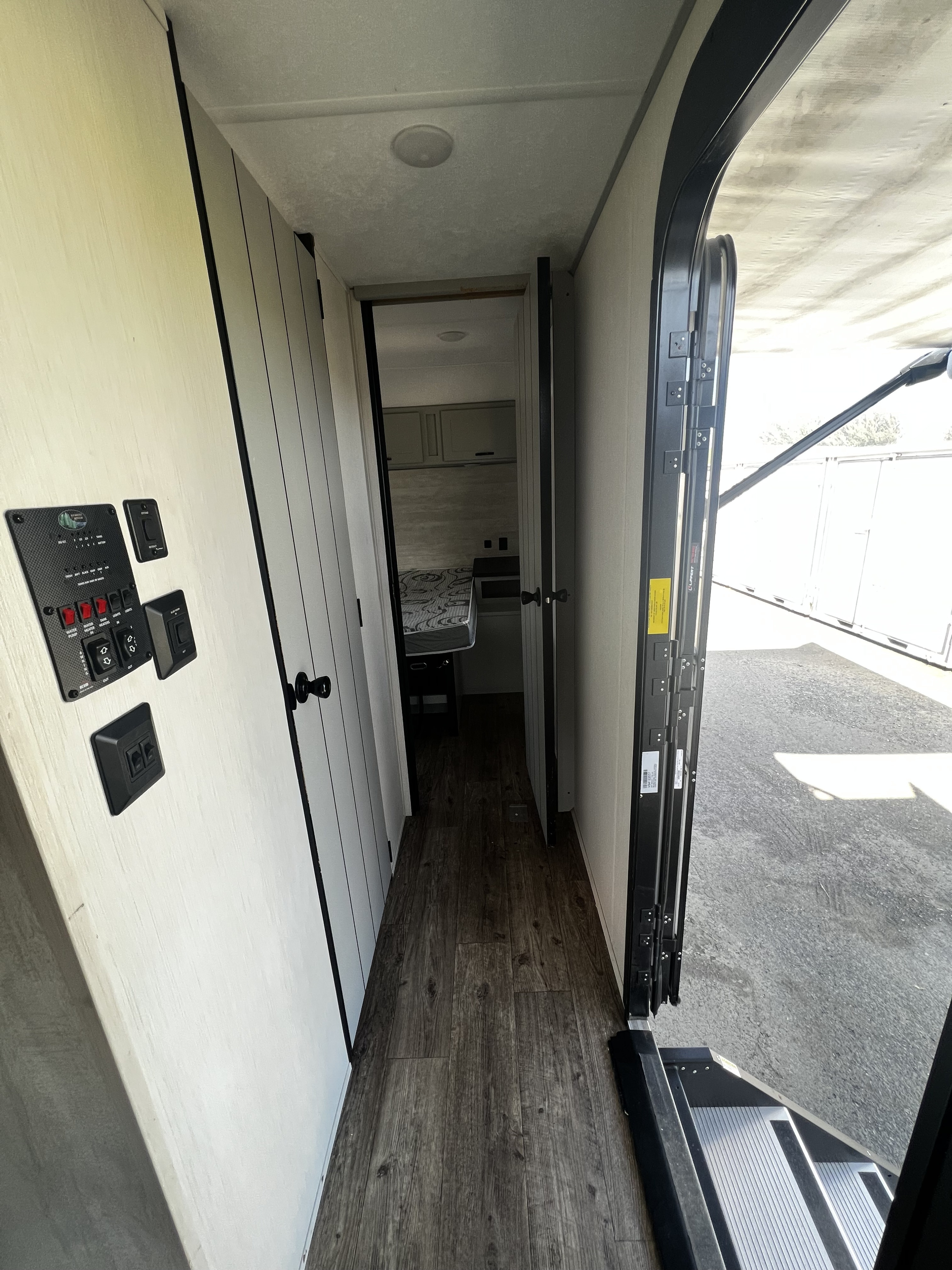 Interior of an RV rental, showcasing a hallway with control panel, dark wood flooring, leading to a bedroom. Open main door.. Forest River Vibe 2022