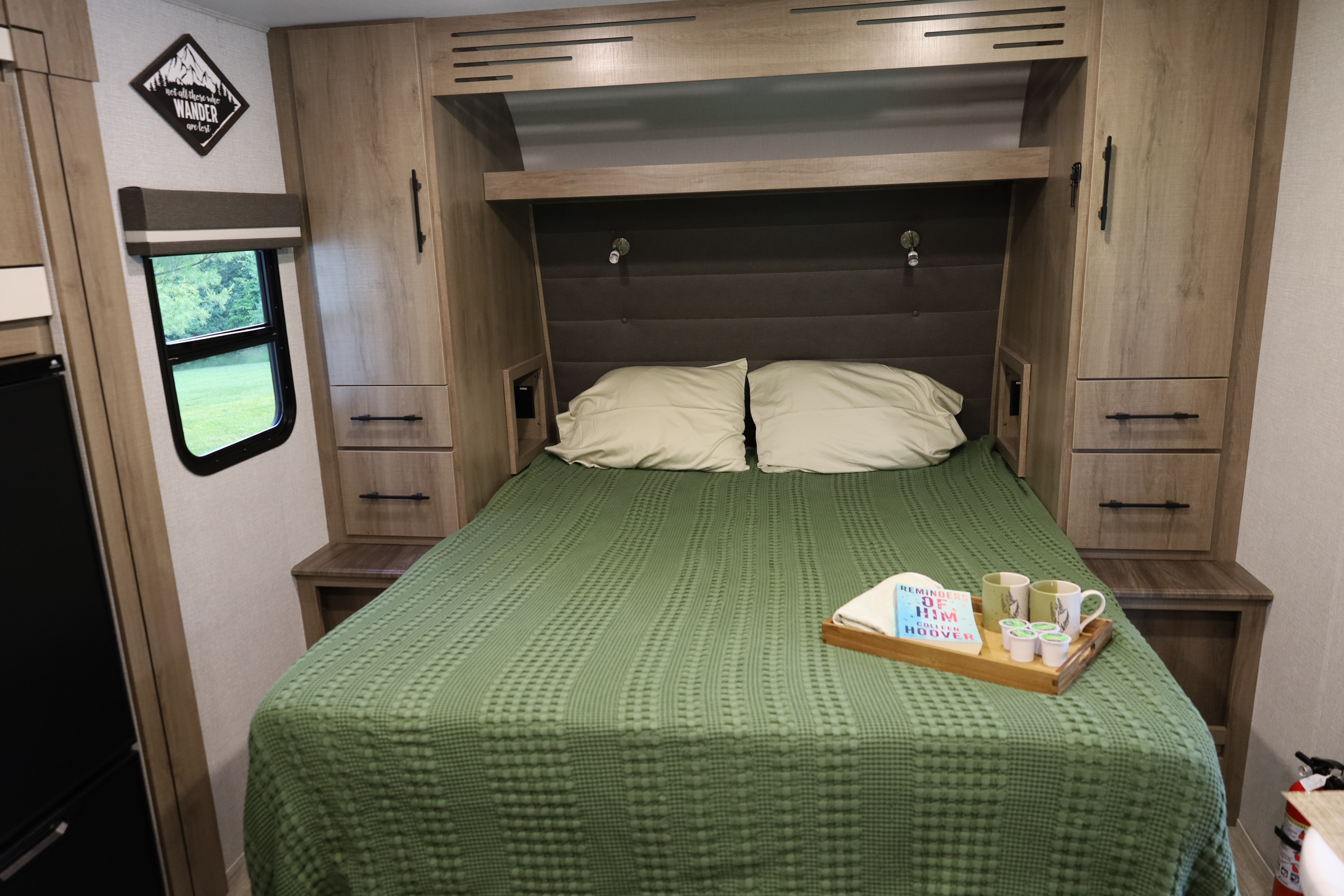 Inviting RV rental bedroom with a comfortable bed, built-in storage, window view, and cozy coffee/book setup.. Grand Design Imagine 2023