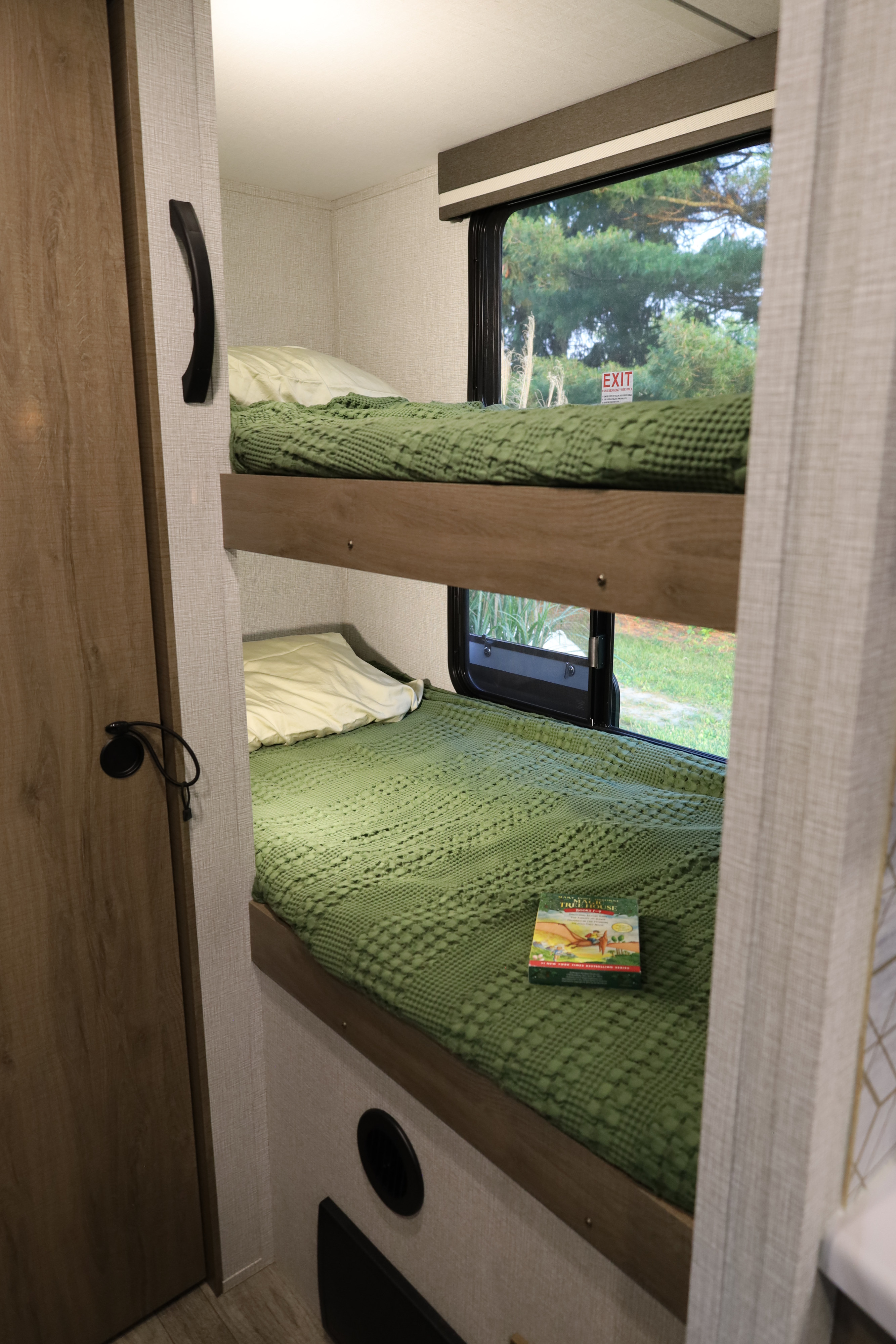 Cozy RV rental interior showing two bunk beds with green blankets, a window view, and a children's book.. Grand Design Imagine 2023