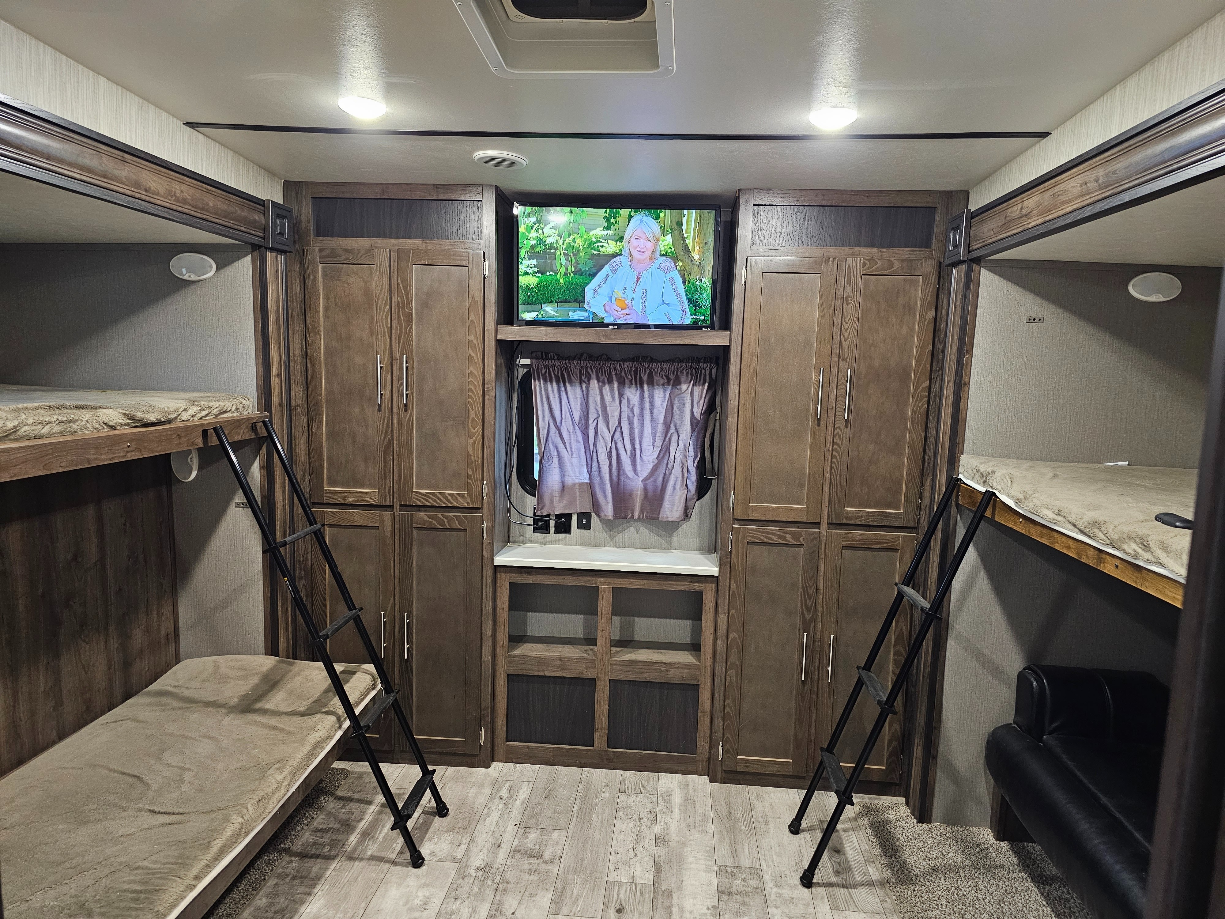 An RV rental interior showing a bunkhouse setup with twin beds, ladders, central TV, and storage for comfortable travel.. Crossroads RV Volante 2019