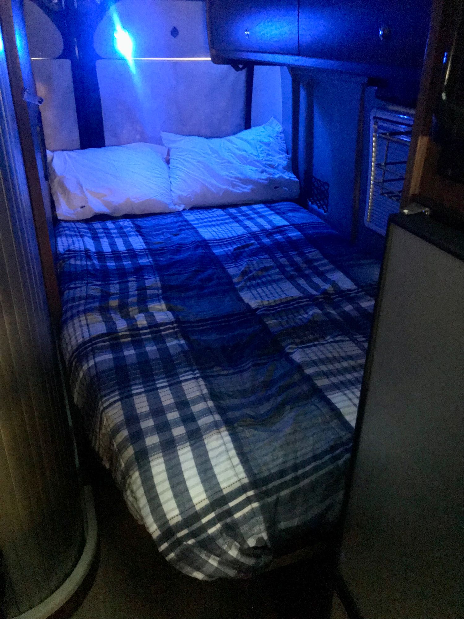 Cozy RV rental bedroom featuring a plaid bed, white pillows, and ambient blue lighting, ideal for travel.. winnebago Travato 59GL 2020