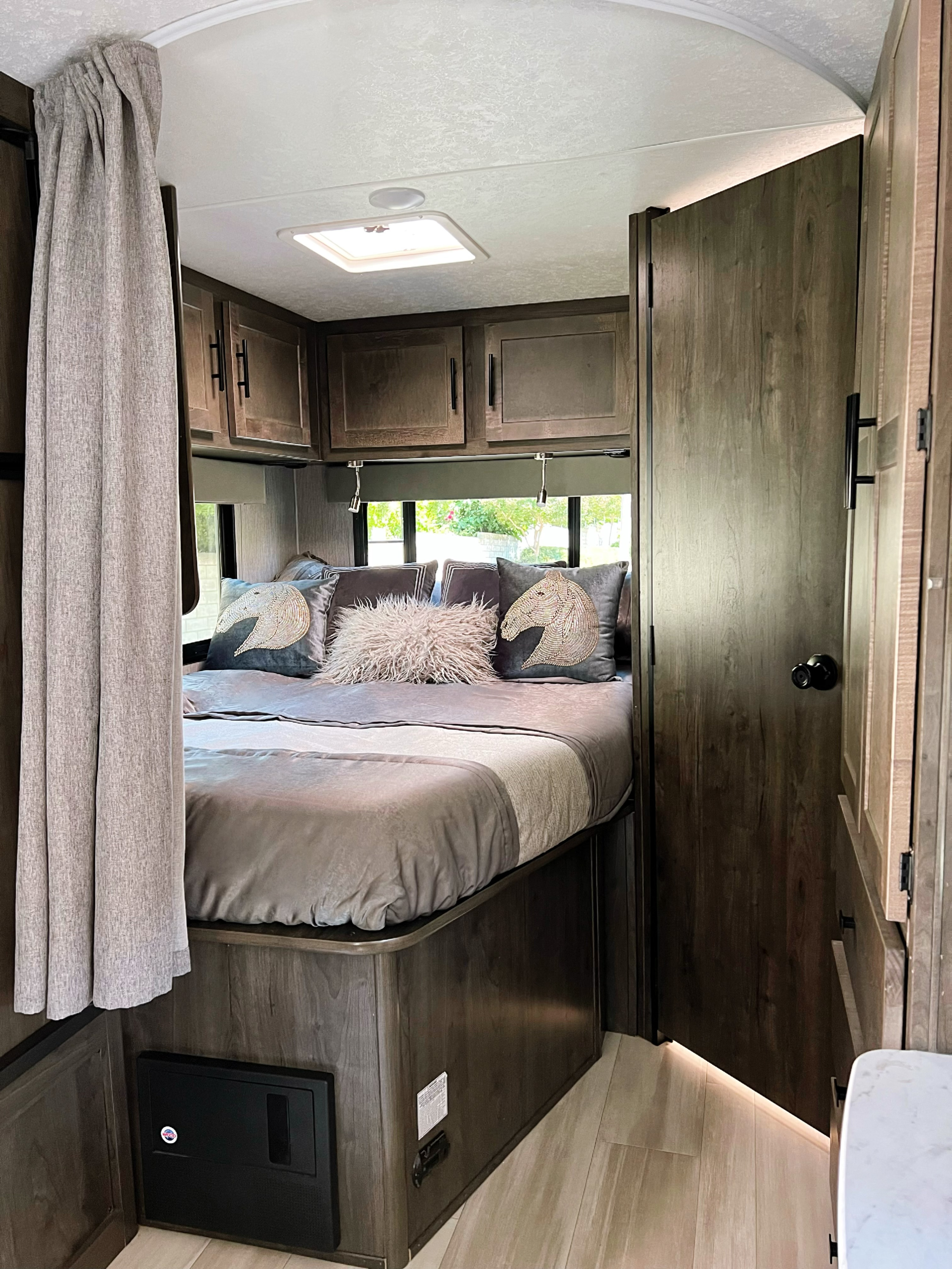 Cozy RV rental bedroom featuring a comfortable bed, wood-tone cabinets, and soft lighting.. Coach House 230BC 2022