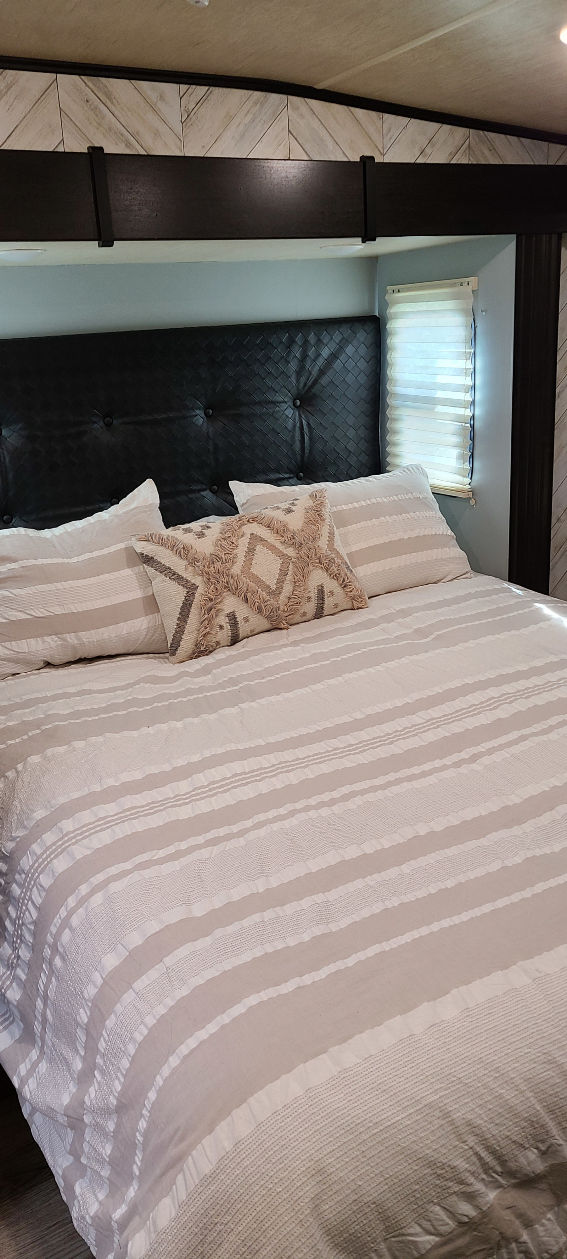 Cozy RV rental bedroom featuring a black woven headboard, striped bedding, and a patterned pillow.. Heartland Road Warrior 2017
