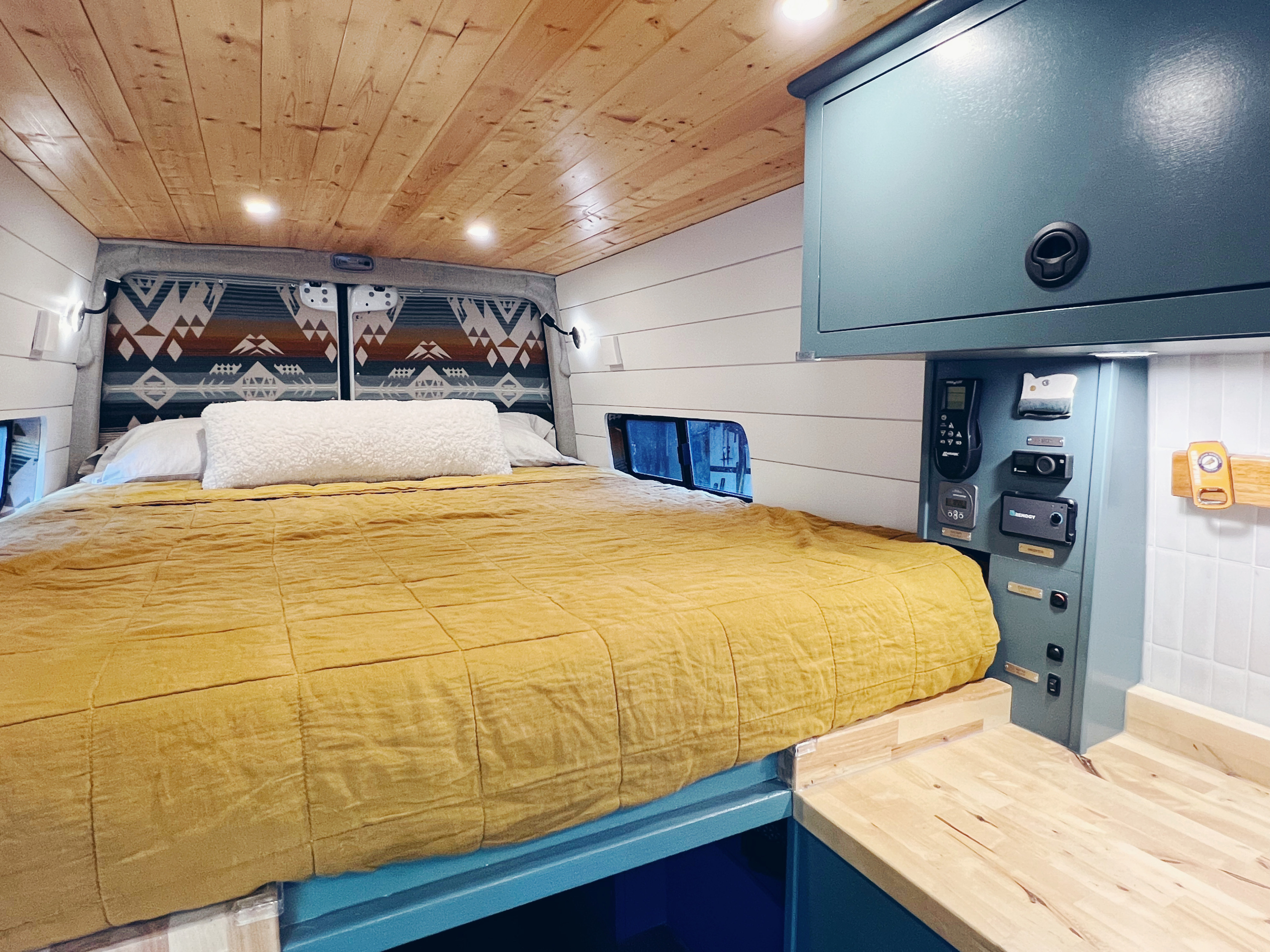 Inside a stylish RV rental: a comfy bed, wood-paneled ceiling, blue cabinets, and convenient controls for your next adventure.. Freightliner Sprinter 2500 2019