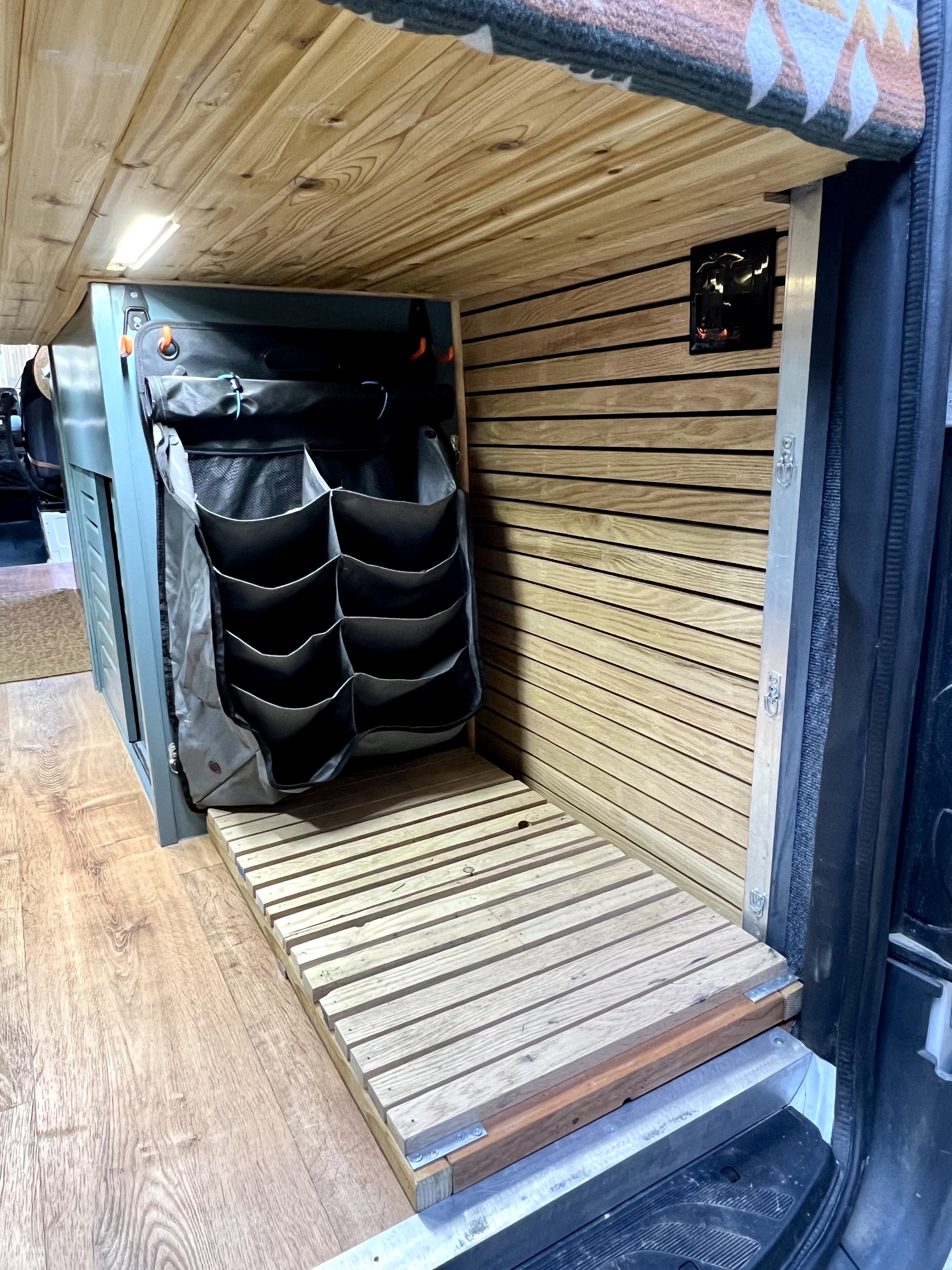 Bright RV rental interior with wooden paneling, hanging storage, and a slatted bed platform, for efficient living.. Freightliner Sprinter 2500 2019
