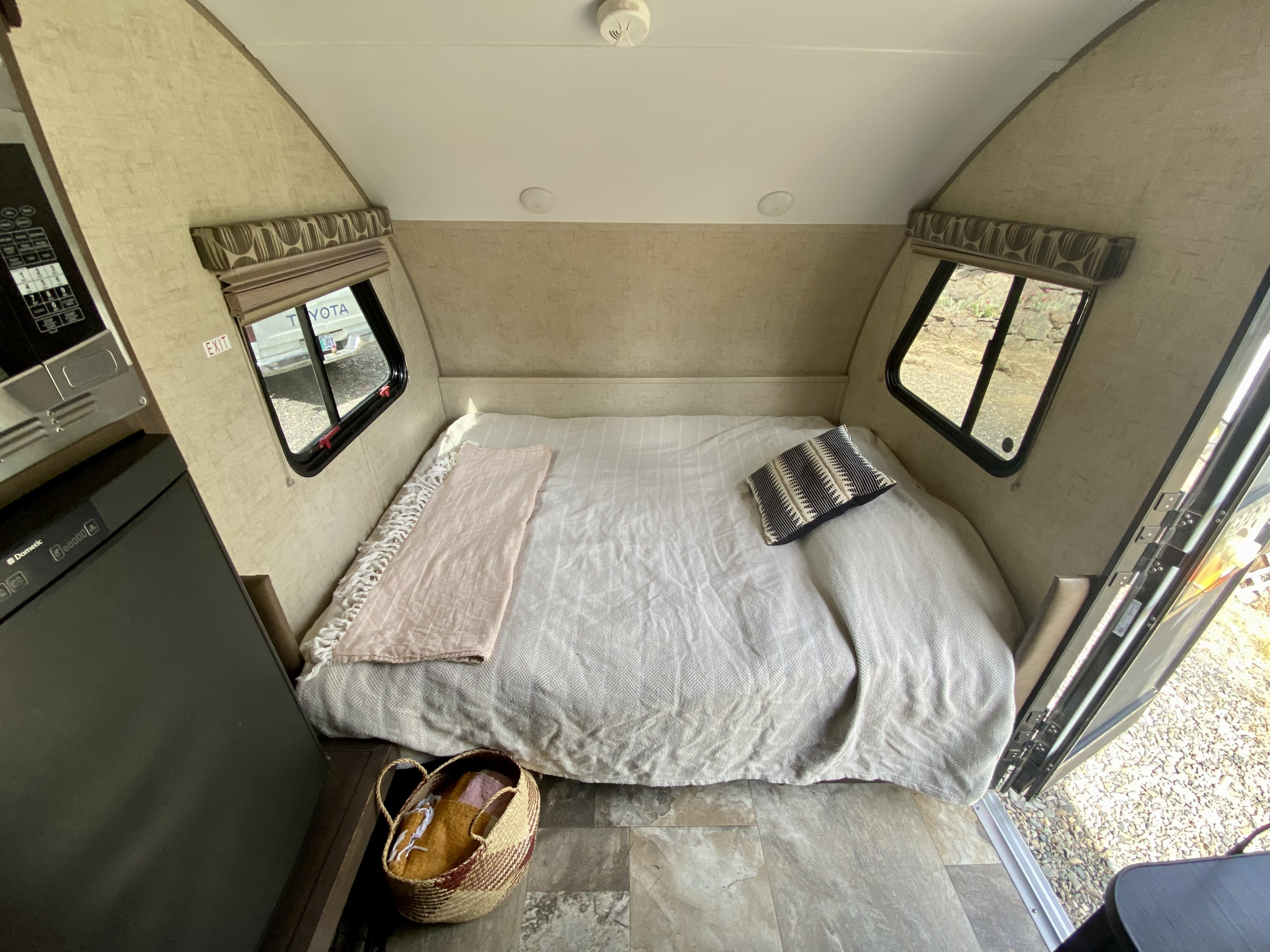 RV rental interior: main bed area with pillows & blankets, integrated microwave/fridge unit, and views through windows/door.. Forest River Rpod-182G 2016