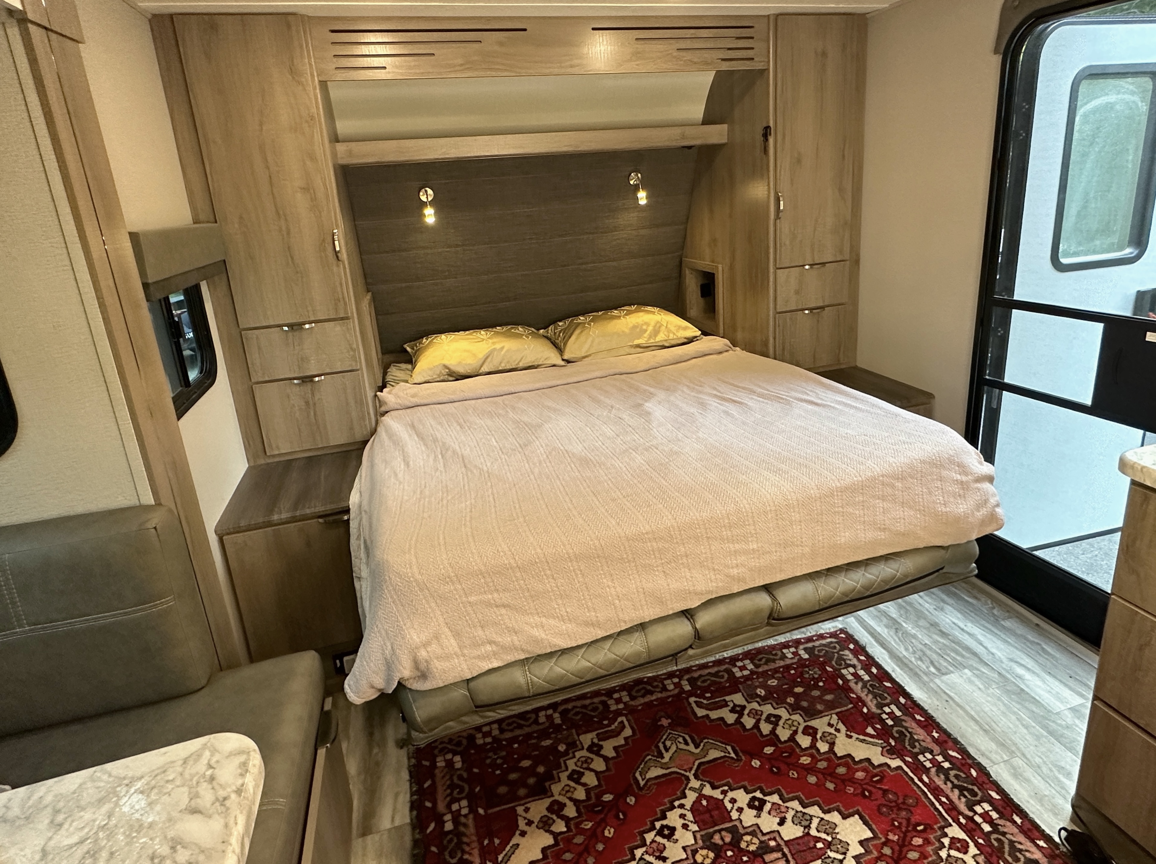 Inside a comfortable RV rental: A bedroom featuring a queen bed, surrounding cabinets, and a bright, compact living space.. Grand Design Imagine XLS 2021