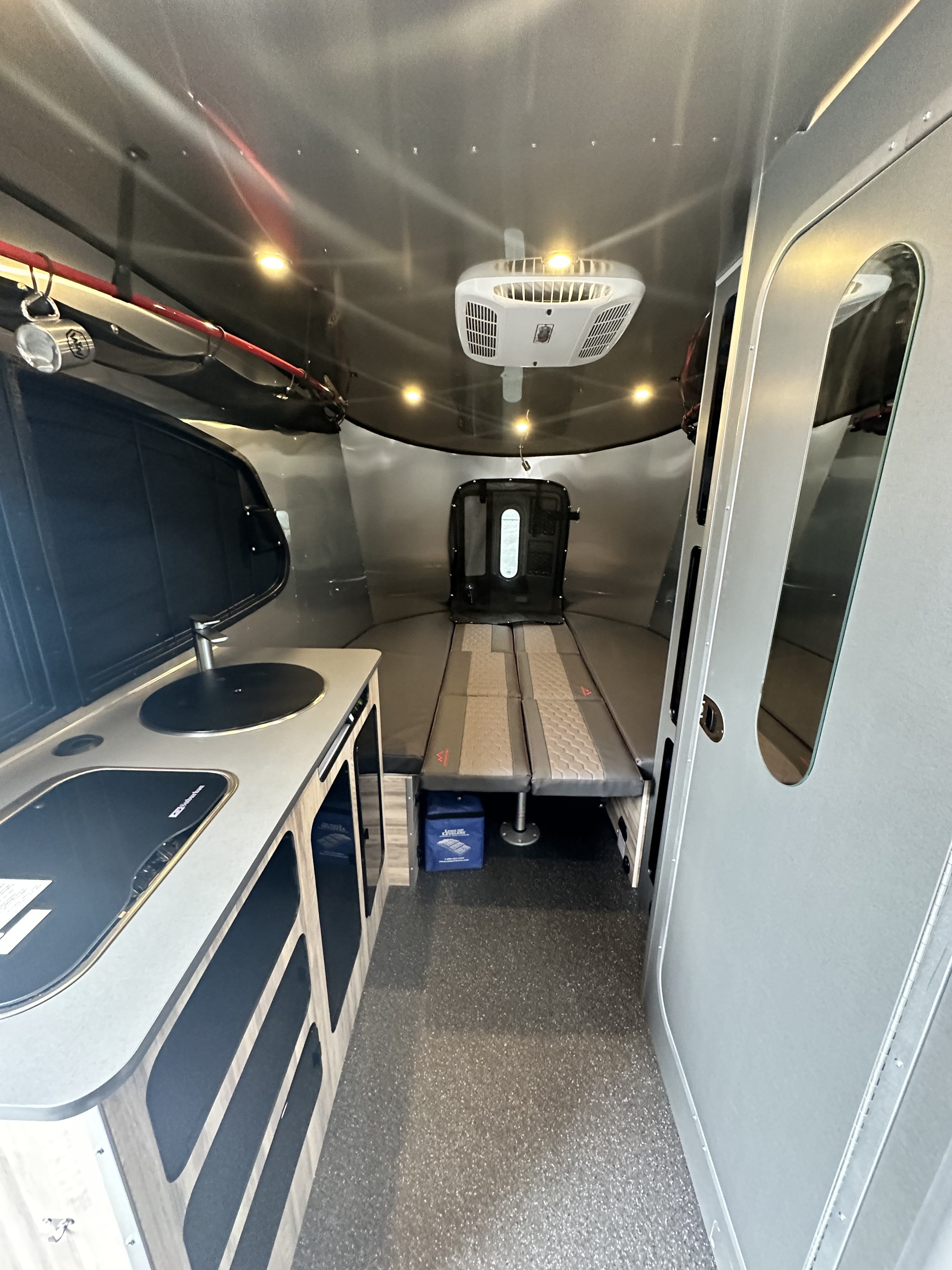 Explore this rv rental's cozy interior, featuring a compact kitchenette, convertible bed, and overhead AC unit.. Airstream Basecamp 20X 2023