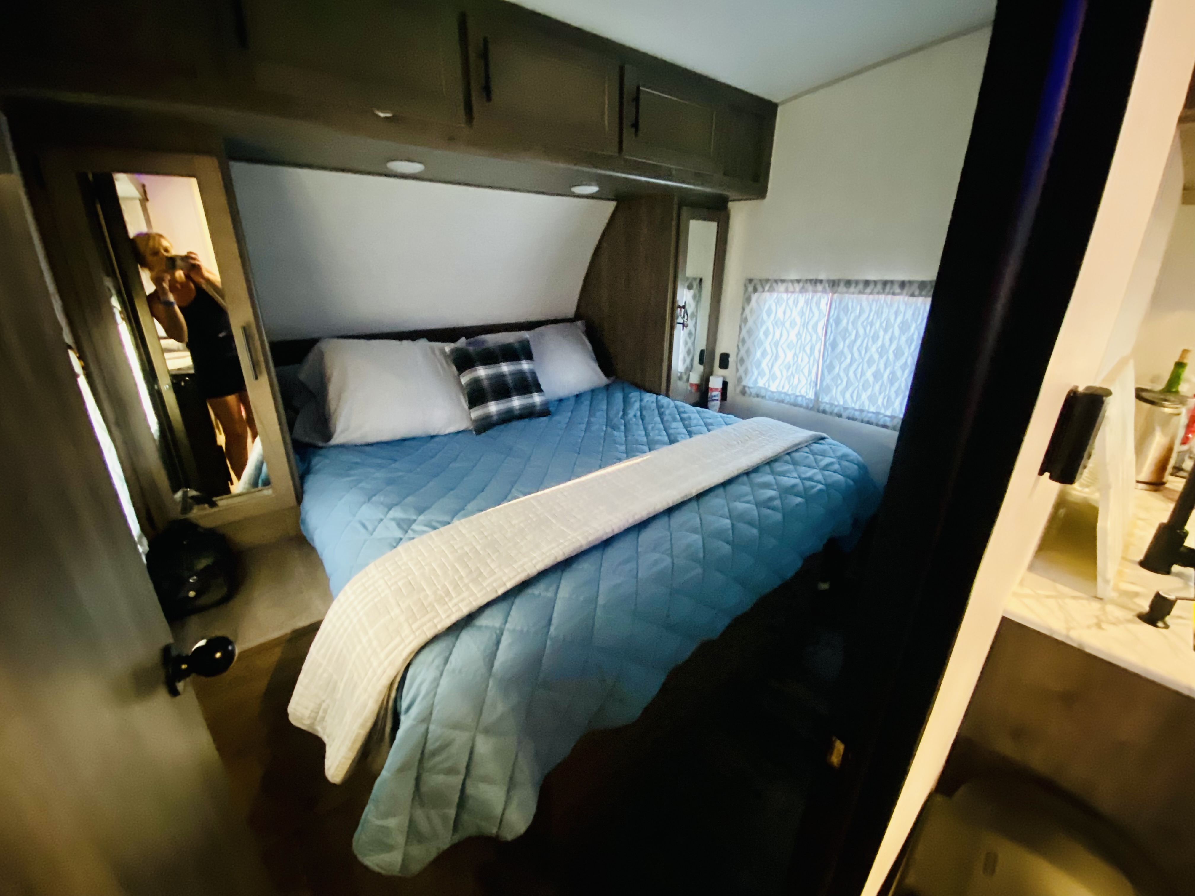Cozy RV rental bedroom features a blue quilted bed, overhead storage, and a mirrored wardrobe, perfect for travel comfort.. Forest River Cherokee Wolf Pack 2022