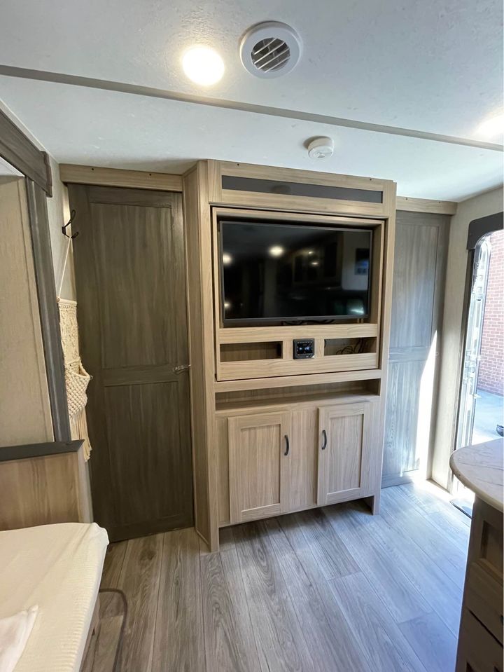RV rental interior: modern light wood built-ins, entertainment center with TV, storage, and wood-look flooring.. Coachmen Freedom Express 2021